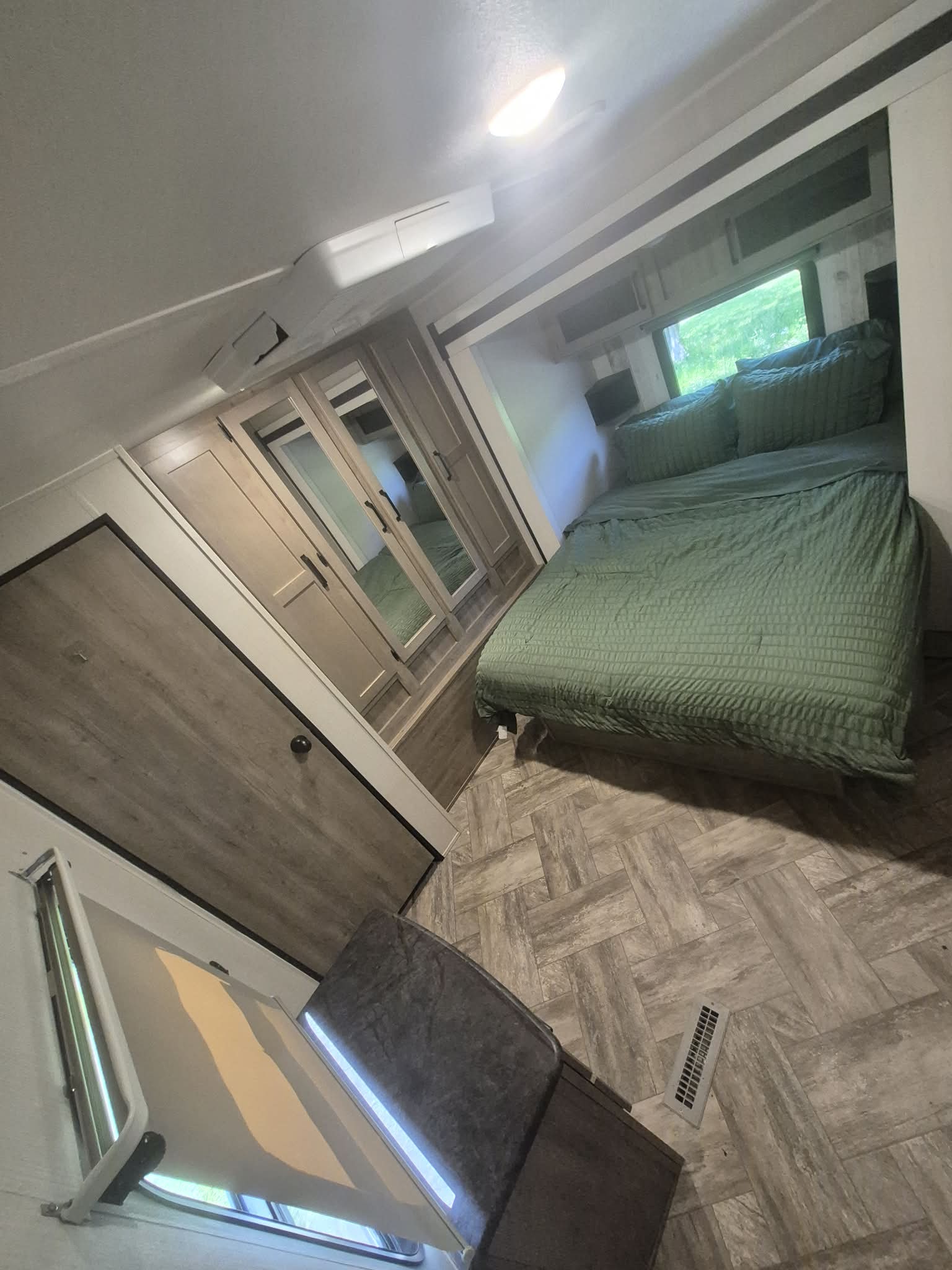 Inside an RV rental bedroom: green bed, mirrored wardrobe, floor vent, and window showing greenery. Compact and comfortable.. palomino puma 2023