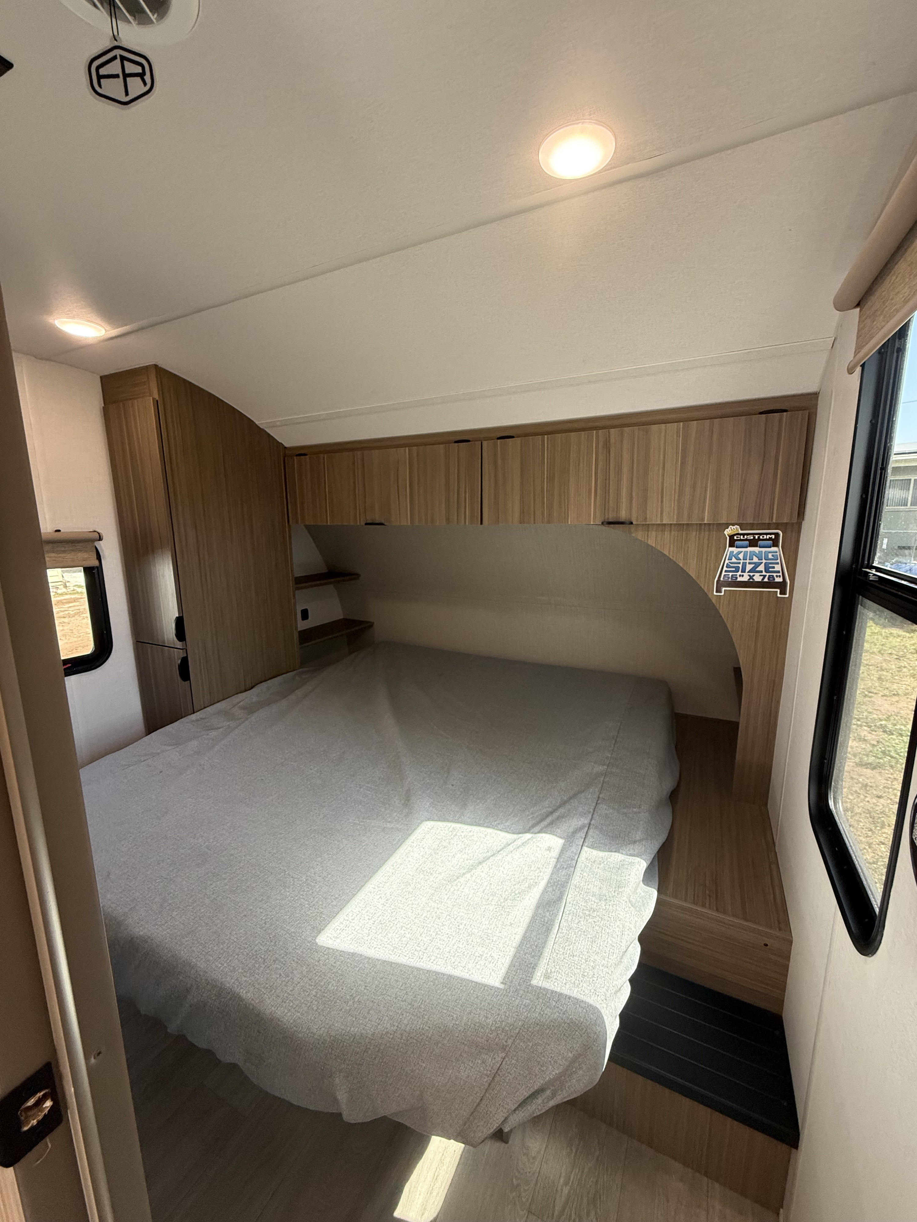 Spacious RV rental bedroom featuring a king-size bed (66"x78"), overhead cabinets, and a window.. Forest River Salem Cruise-Lite 2026