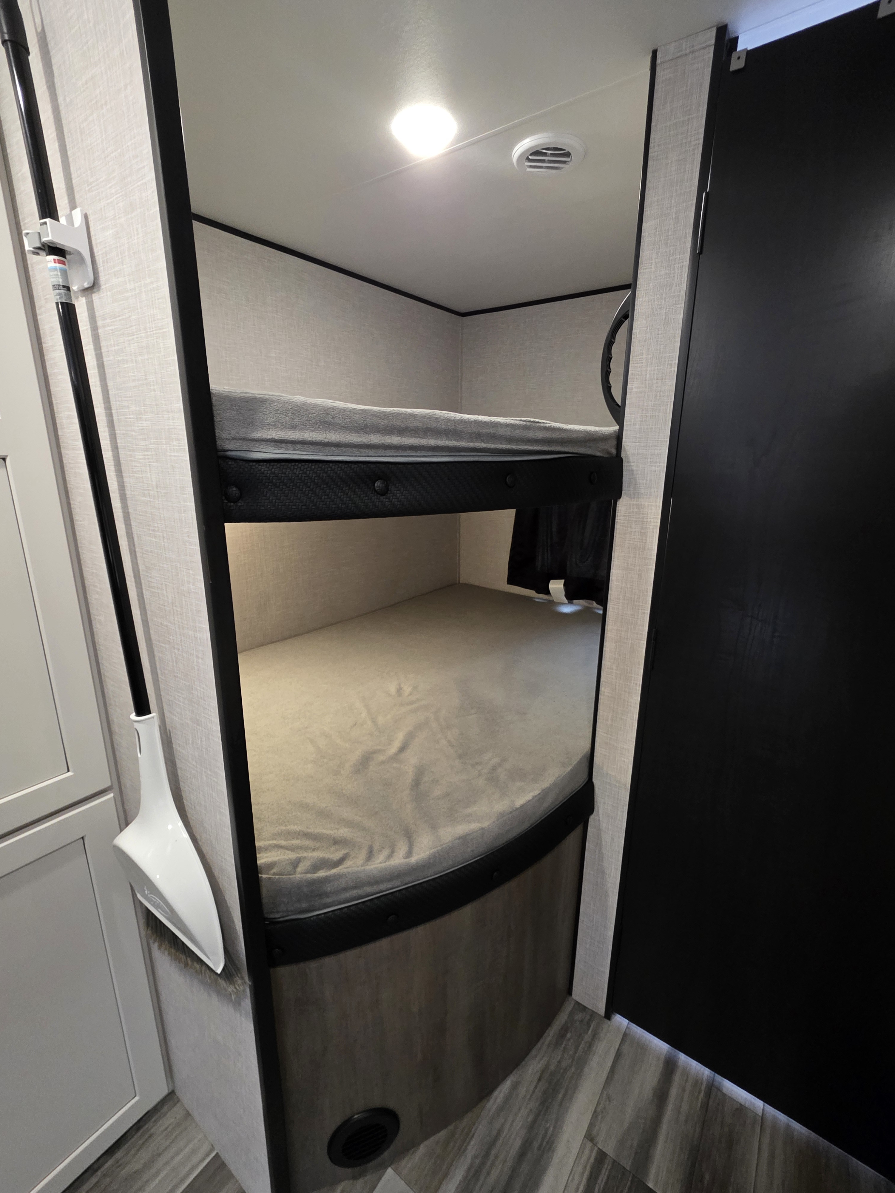RV rental with bunk beds. A broom and dustpan hang on the wall, with a ceiling light and vent visible above.. Jayco Jay Flight SLX 2025
