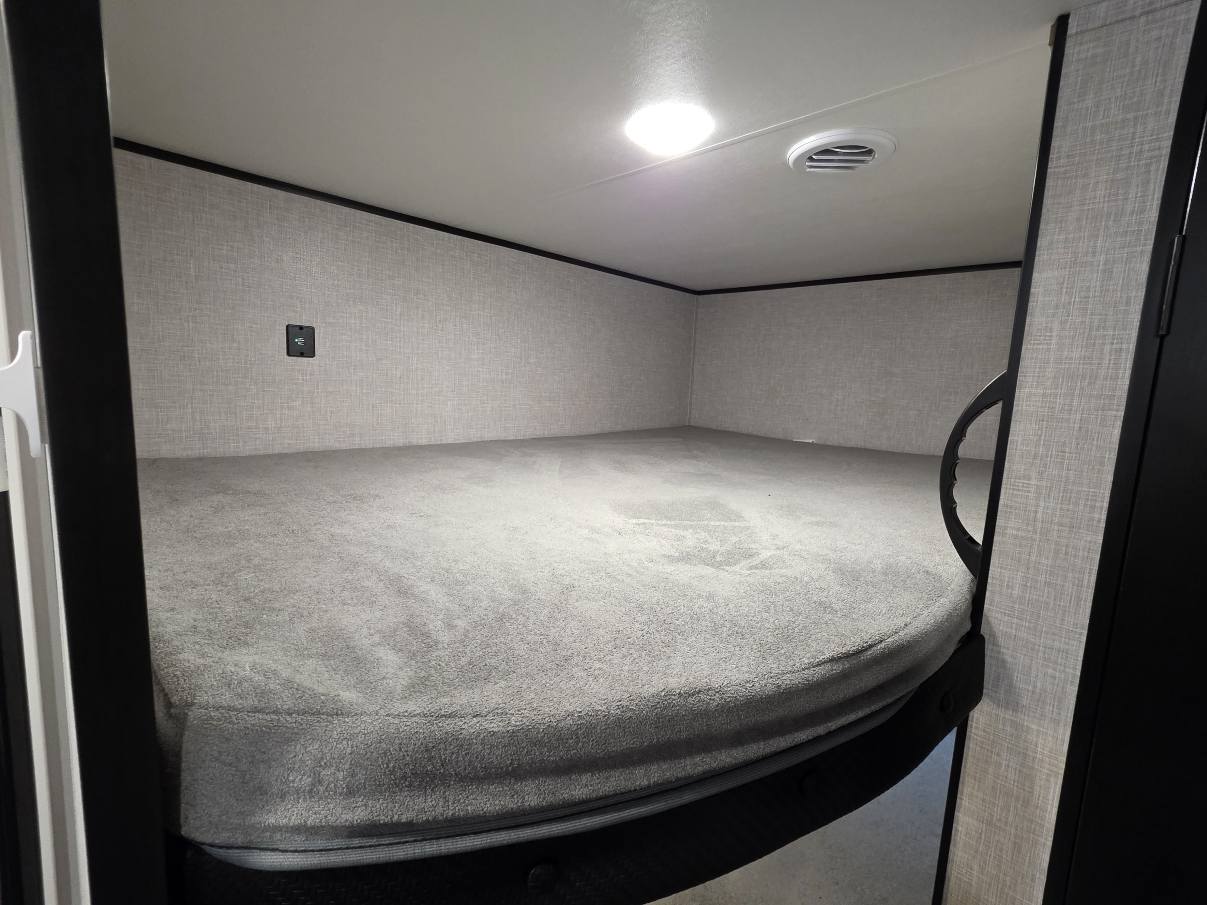 RV rental bunk bed: a cozy sleeping area with a soft grey mattress, wall-mounted USB charger, ceiling light & vent.. Jayco Jay Flight SLX 2025