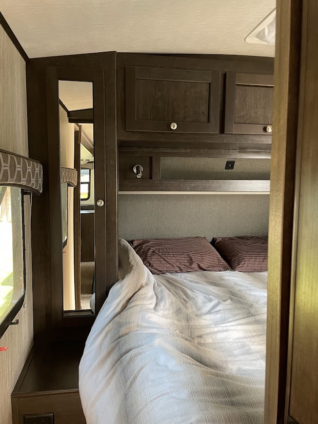 Cozy RV rental bedroom with dark wood cabinets, a mirror, and a comfy bed. Enjoy this compact sleeping area.. Cruiser RV Shadow Cruiser 2020