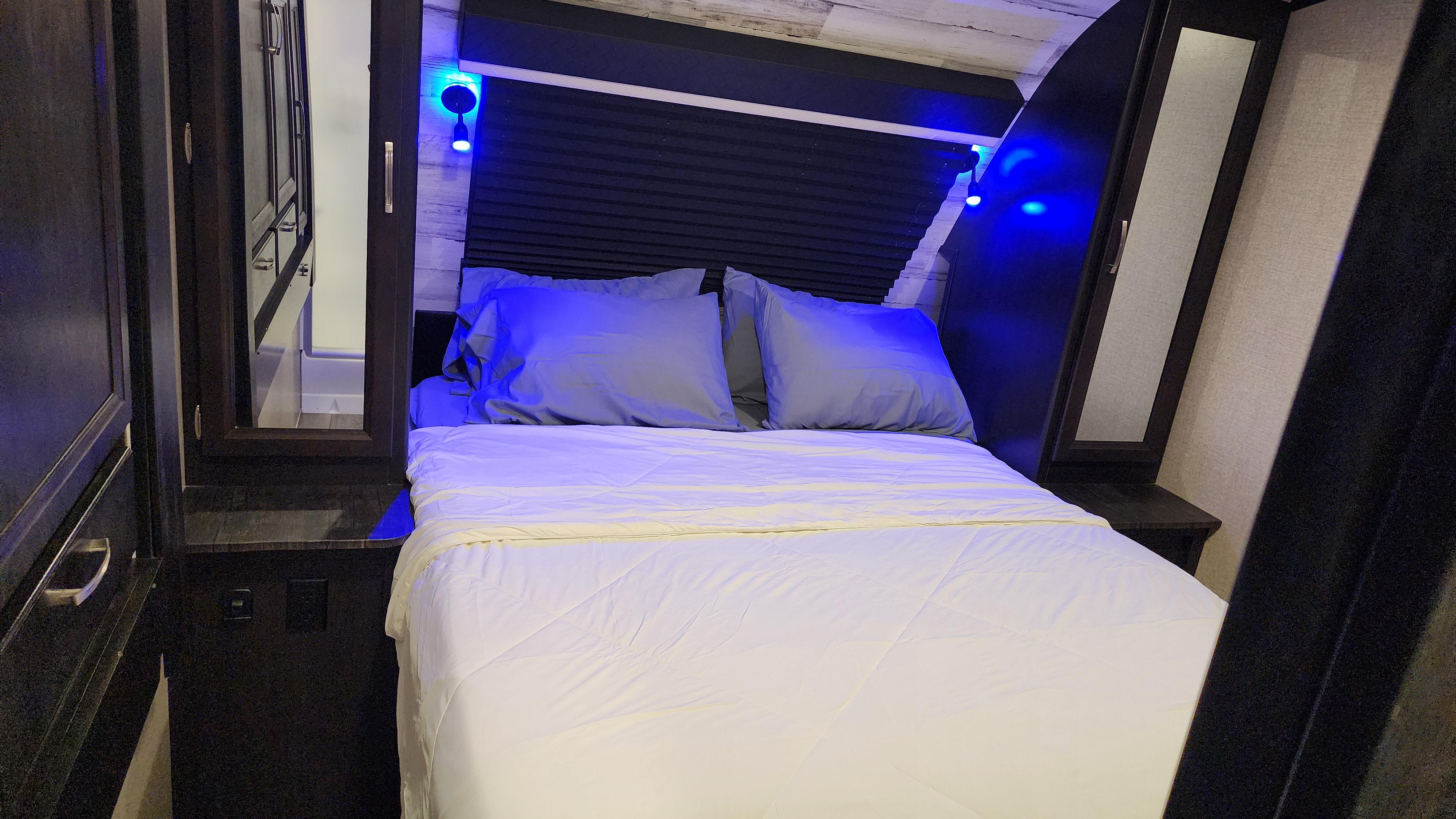 Cozy RV rental bedroom featuring a comfortable bed, blue accent lighting, compact storage, and reflective surfaces.. Jayco White Hawk 2020