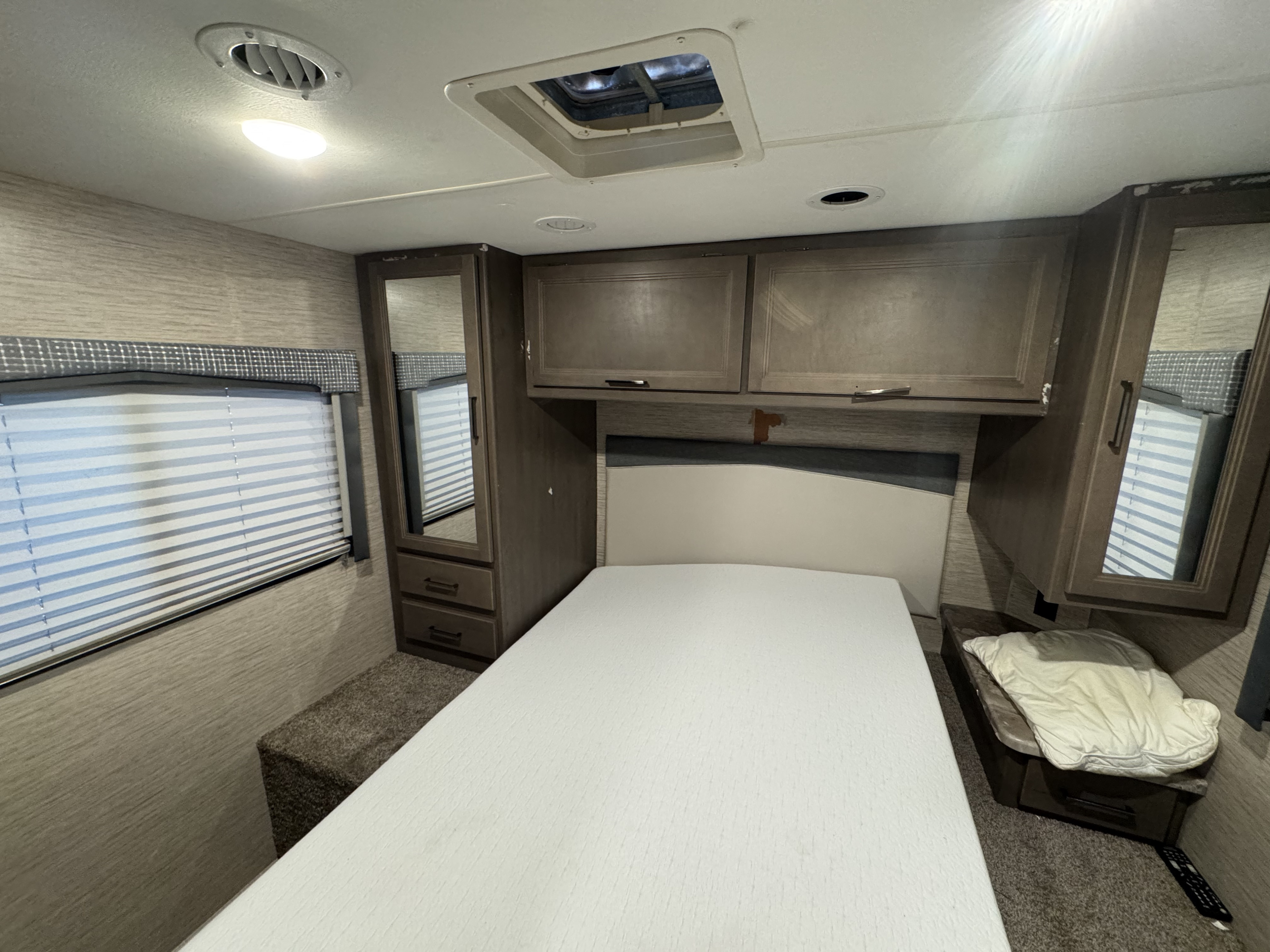 Cozy RV rental bedroom with a white bed, overhead storage, mirrored wardrobe, window, and ceiling vents for comfortable travel.. Thor Chateau 2023