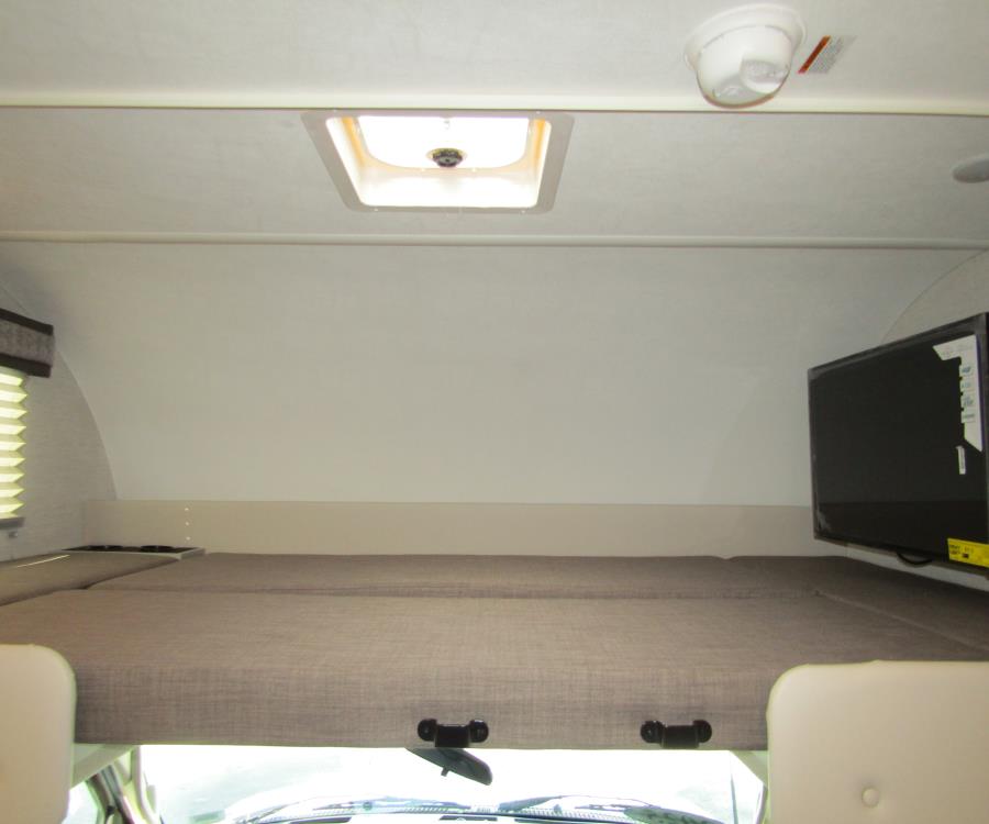 Overhead bunk bed with a ceiling vent, mounted TV, and front view of an RV rental, offering comfortable sleeping quarters.. Thor Chateau 2025