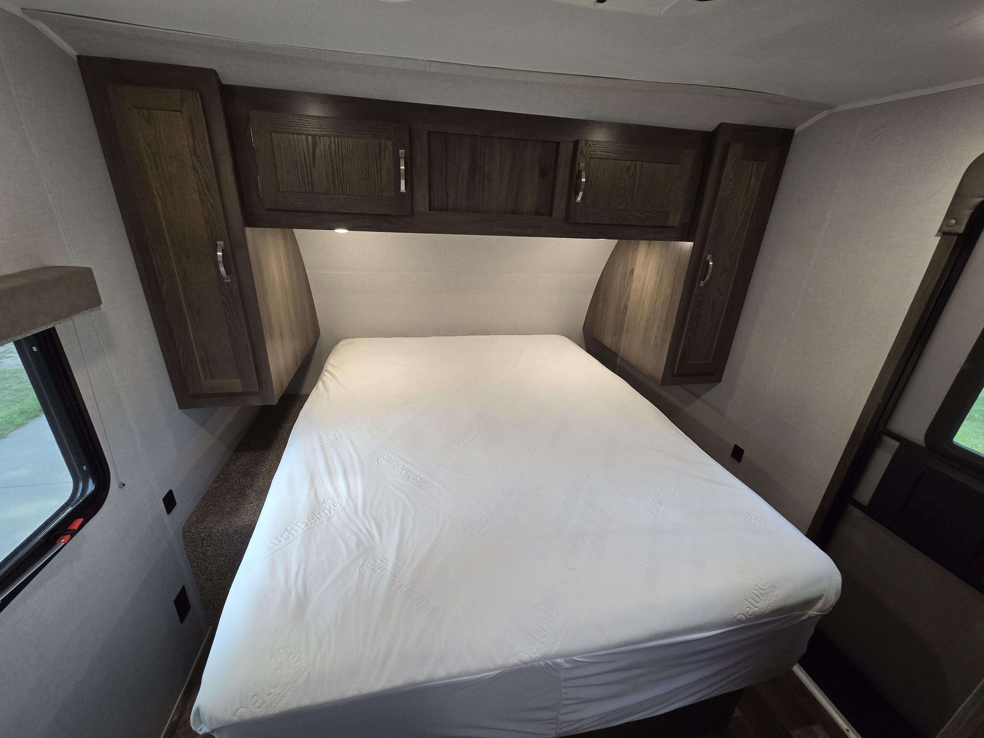 Comfortable RV rental bedroom featuring a "Plush Deluxe" mattress, overhead storage cabinets, and side windows.. Forest River Silver Lake East-West 2020