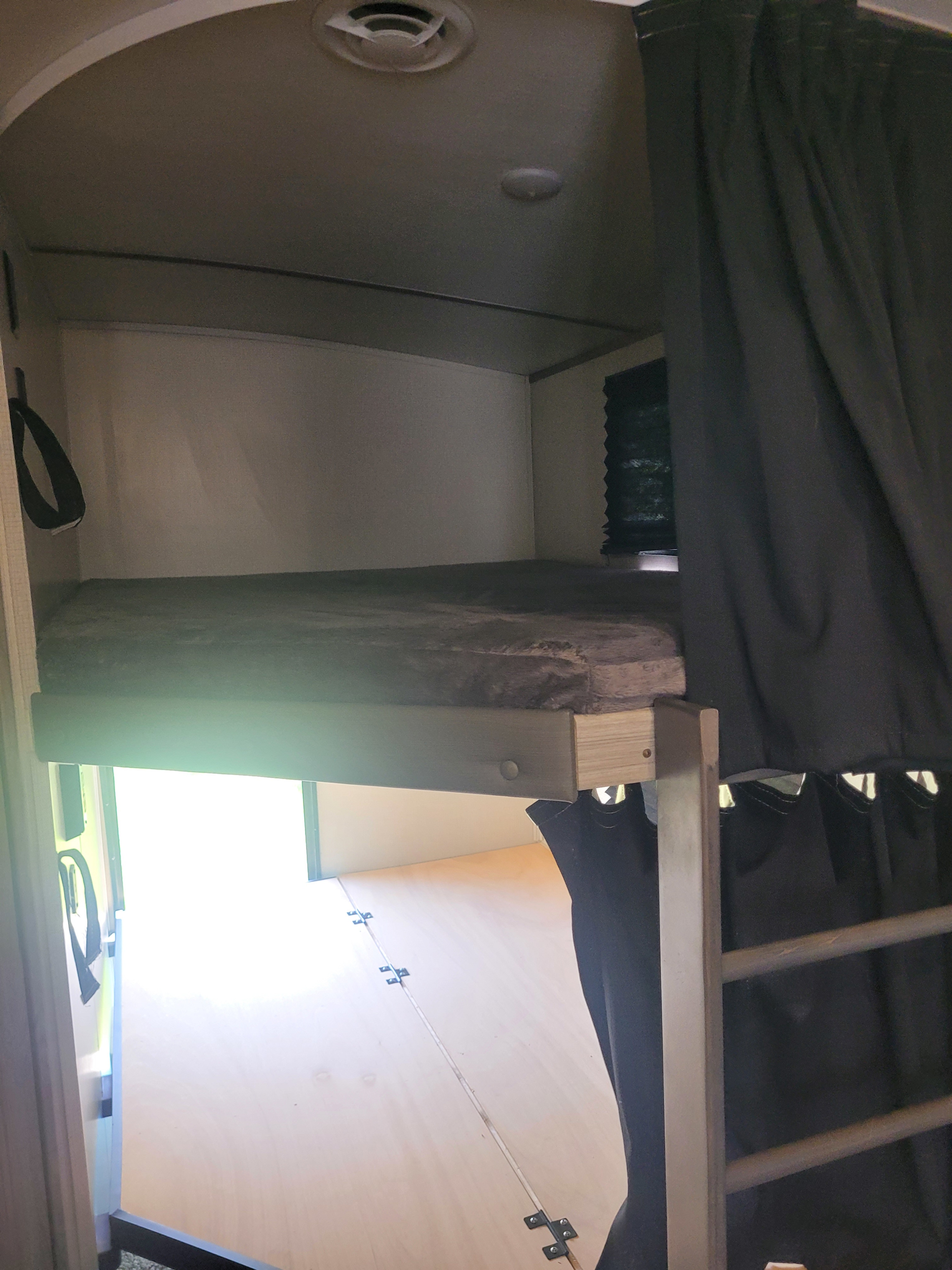 Compact RV rental interior features a bunk bed with dark privacy curtain, overhead vent, and light fixture.. Keystone RV Passport GT 2022