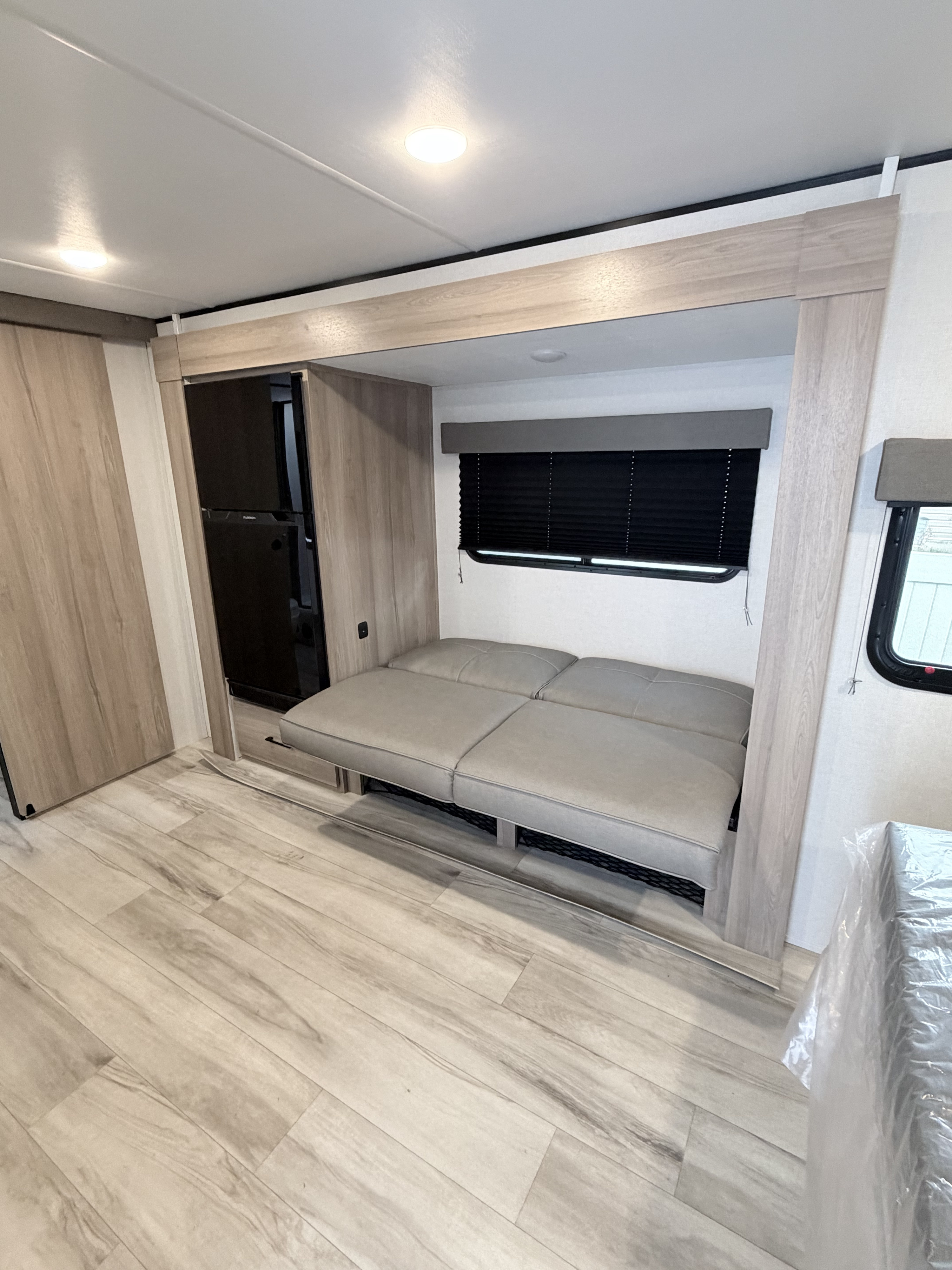 Bright RV interior with a fold-out sofa, fridge, and light wood flooring, ready for your next rv rental trip.. Keystone RV Coleman Light 2025