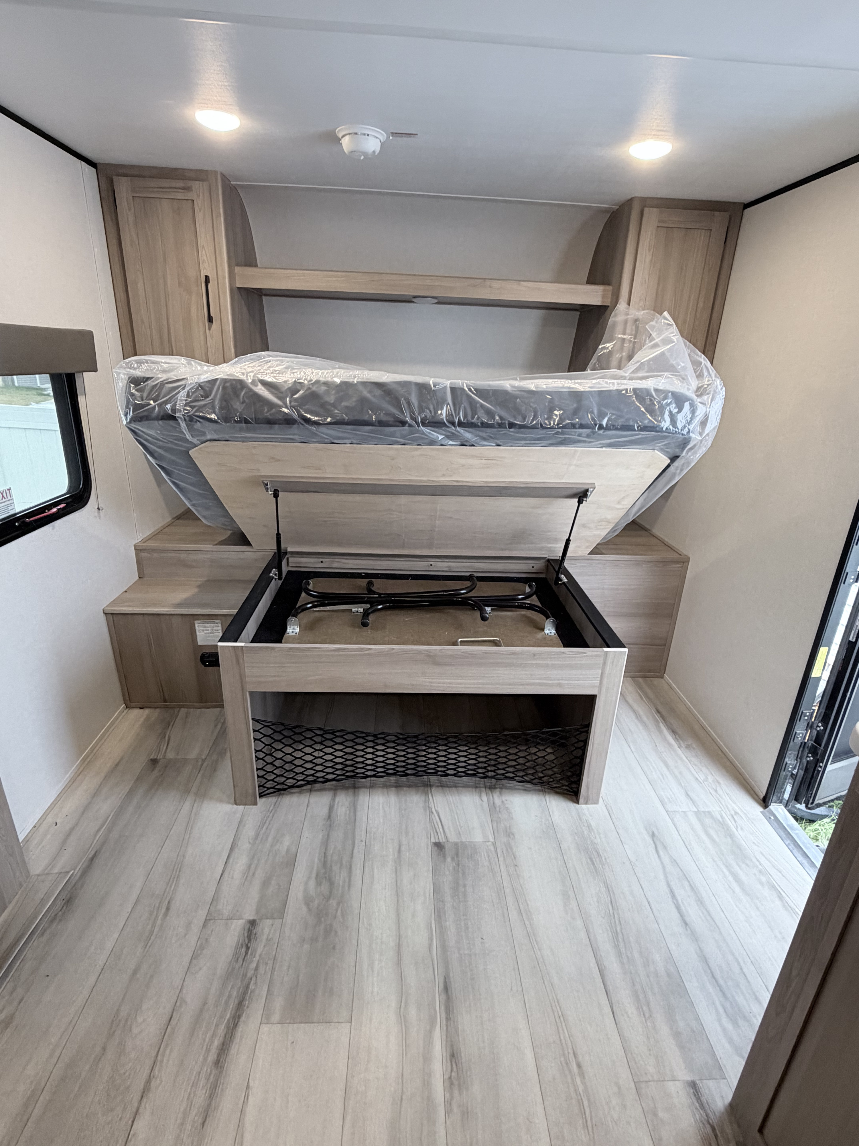 Explore this rv rental's interior: a fold-up bed revealing under-bed storage, surrounded by cabinets and a window.. Keystone RV Coleman Light 2025