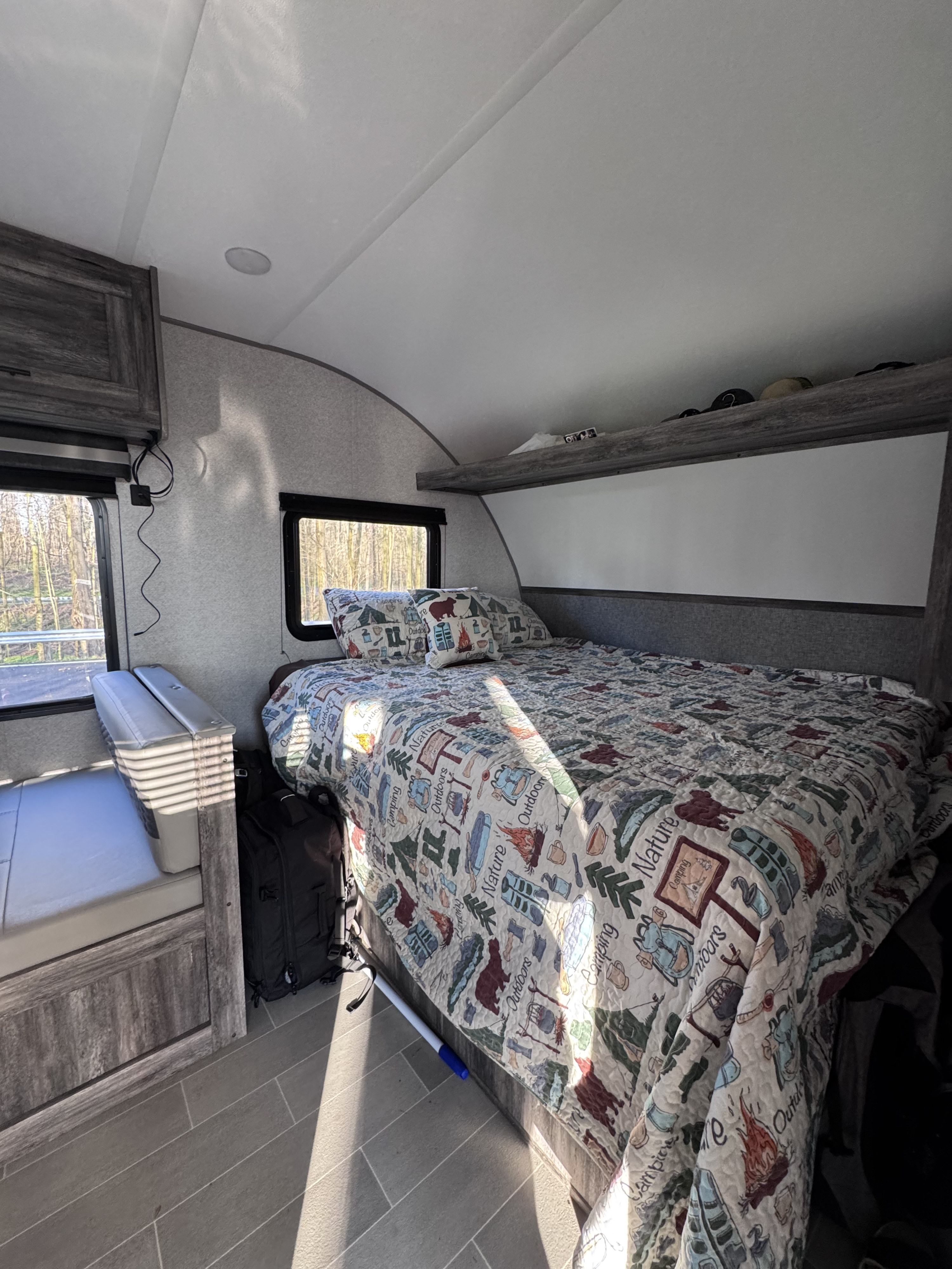 Cozy RV rental interior: bedroom with nature-themed bedding, windows with outdoor views, and a bench seating area.. Forest River Salem FSX 2020