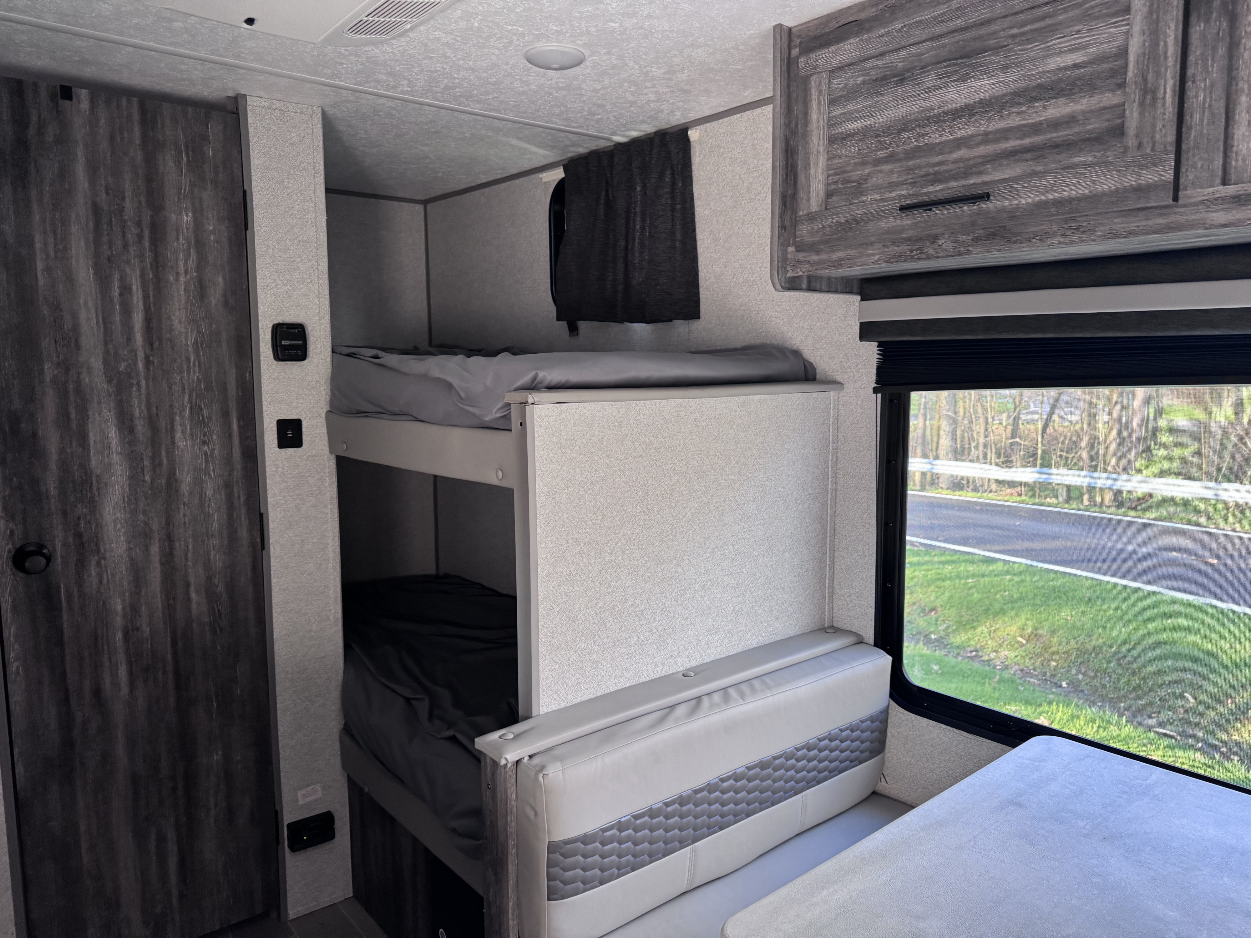 Cozy RV rental interior showing bunk beds with grey bedding, a dinette, and a window overlooking a road.. Forest River Salem FSX 2020