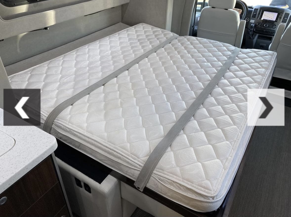 RV rental bed: Quilted mattress with securing straps in a compact RV interior, ready for a comfortable night's sleep.. Airstream Atlas 2018