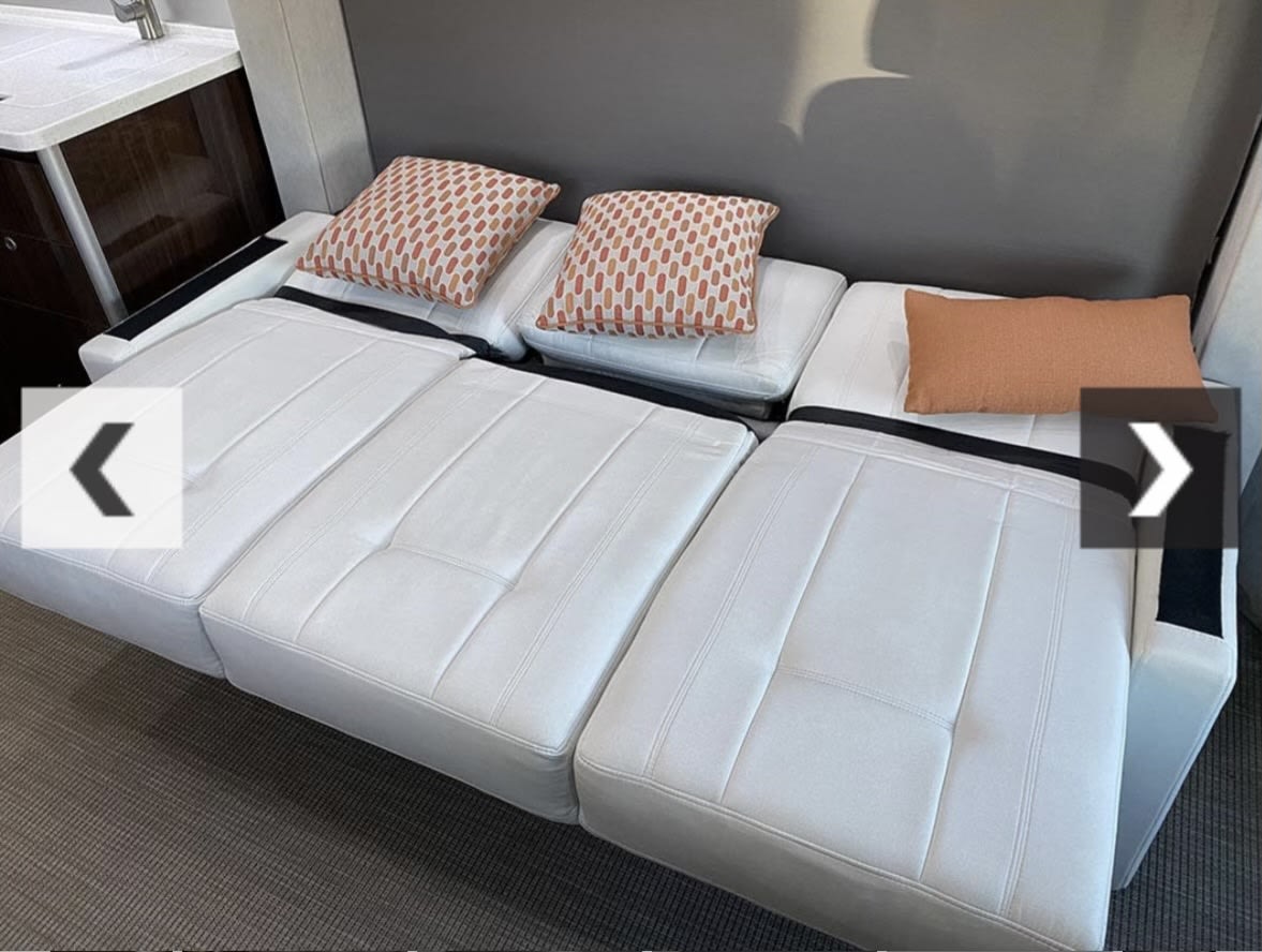 This RV rental features a white convertible sofa bed with accent pillows, offering versatile seating and comfortable sleeping space.. Airstream Atlas 2018
