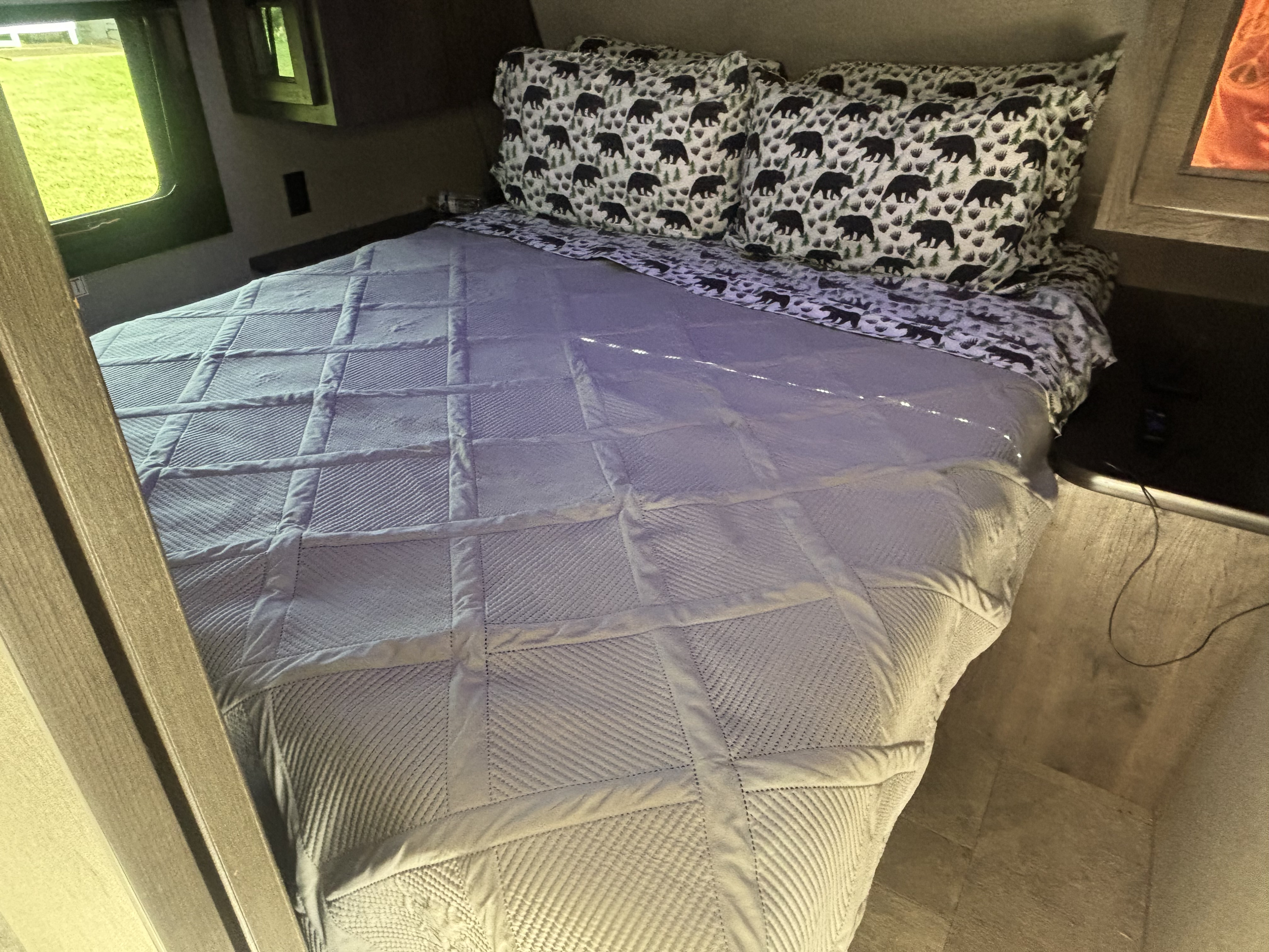 Cozy bed in an RV rental, featuring bear-patterned pillows, a quilted blanket, and a view of green outside.. Jayco Jay Flight 2020