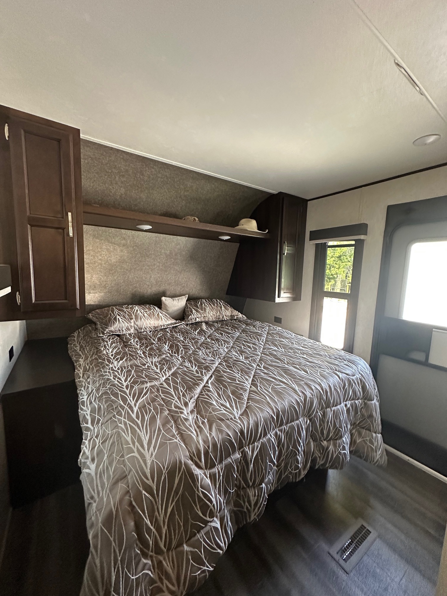 Cozy RV rental bedroom with a large bed, dark wood cabinetry, overhead storage, and natural light from a window.. Jayco Jay Flight SLX Rocky Mountain Edition 2020