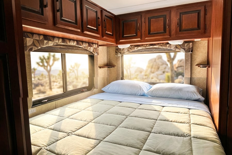 Cozy RV rental bedroom with a comfy bed and a sun-drenched desert view, featuring Joshua trees and rock formations.. Forest River Sunseeker 2012