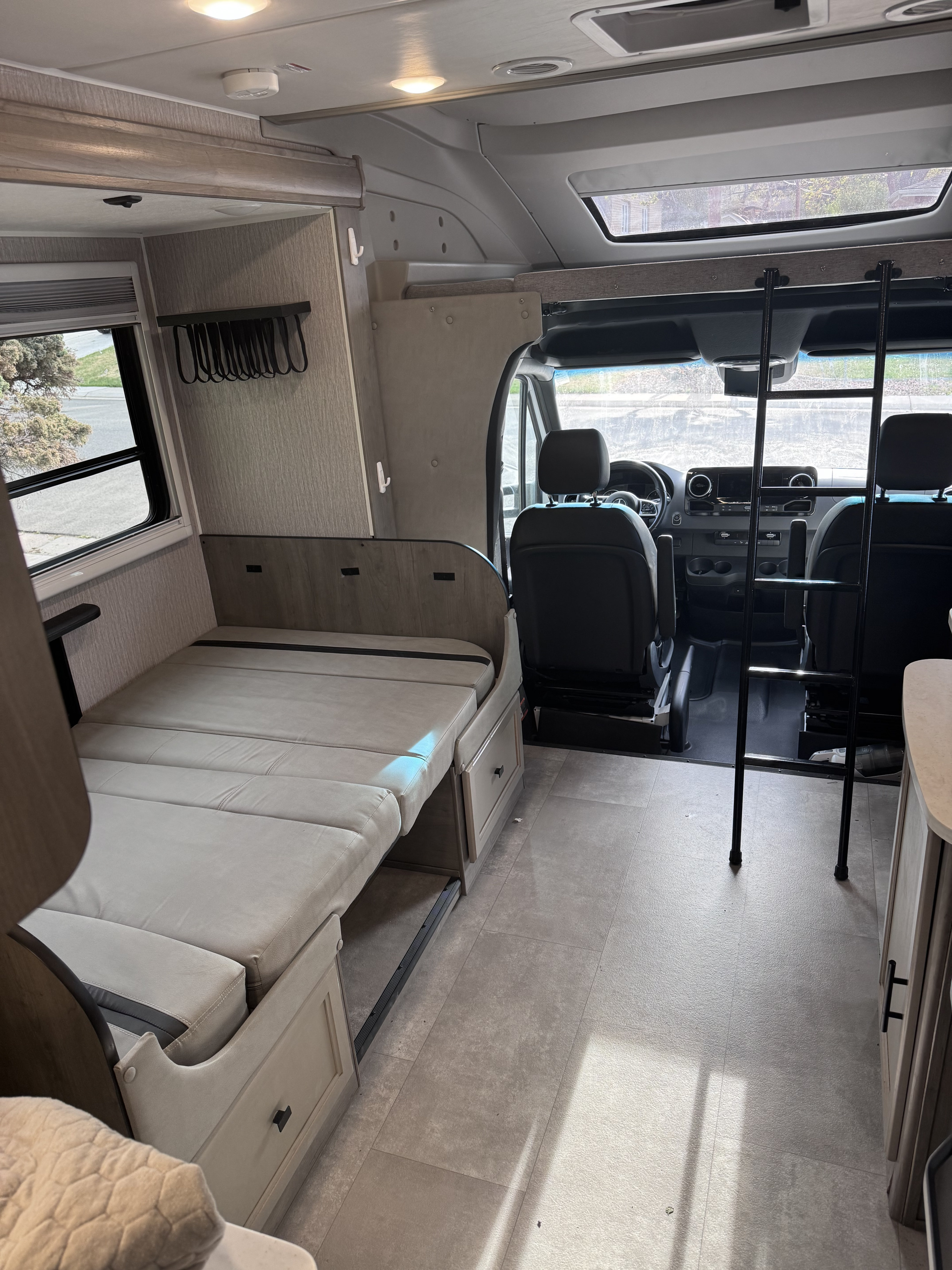 Bright rv rental interior showing a convertible bed with drawers, a front cab, and a ladder to an overhead bunk.. Forest River Coachmen Prism Elite 2022