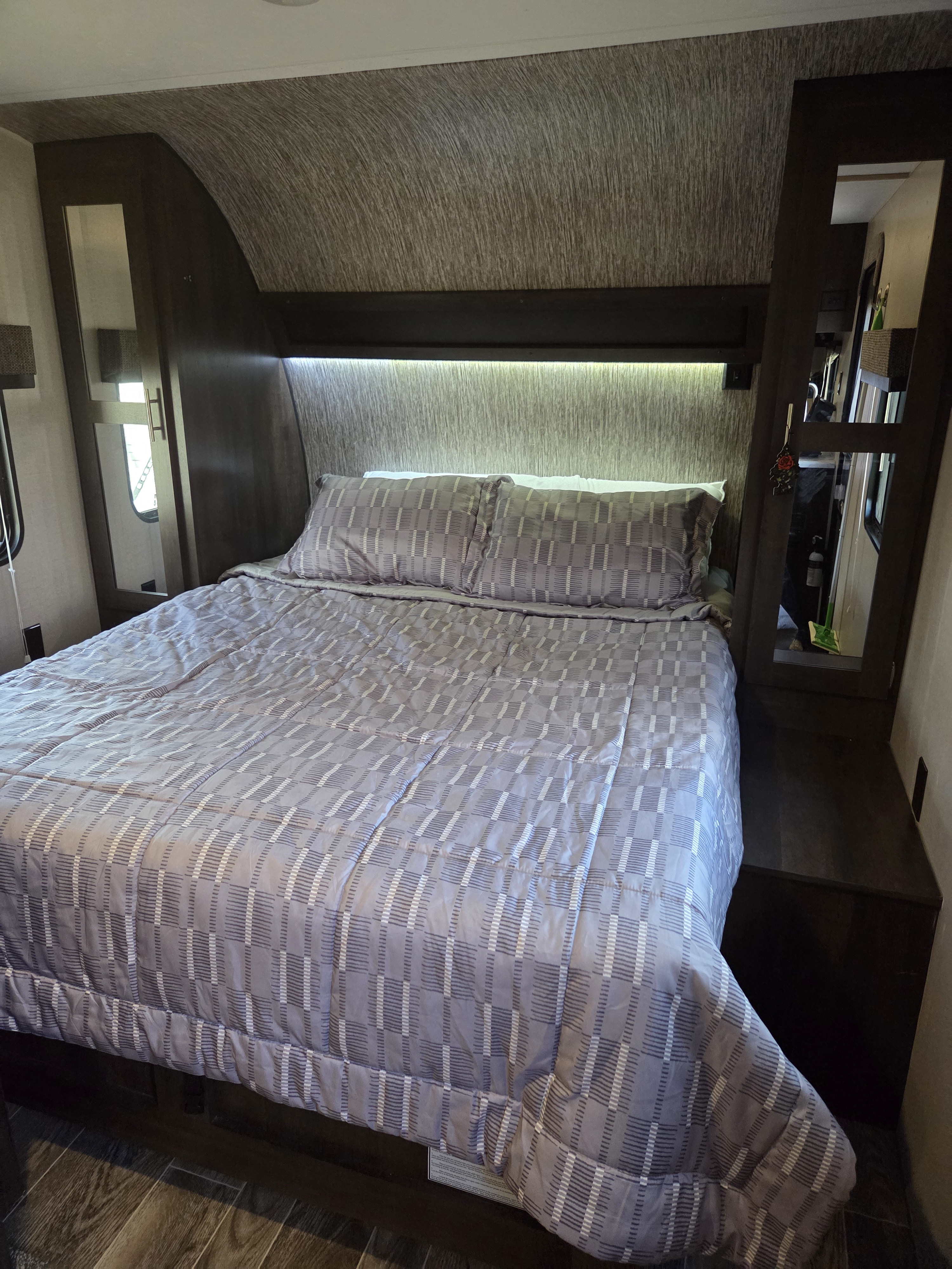 Cozy RV rental bedroom with a neatly made bed, patterned bedding, integrated lighting, and mirrored storage.. Sportsmen LE 2018