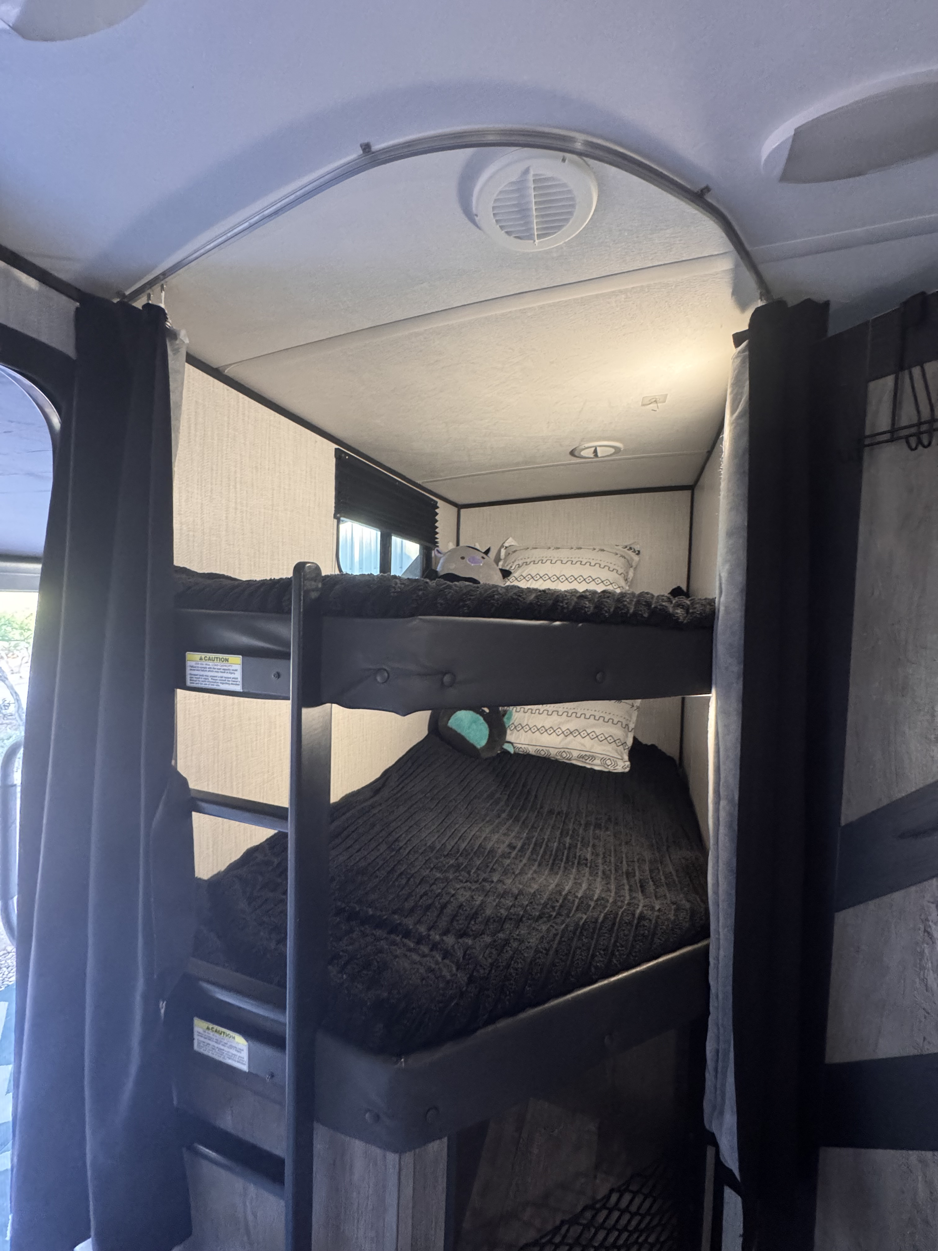 Cozy bunk beds inside an RV rental, featuring dark bedding, patterned pillows, and privacy curtains for travelers.. Heartland RVs North Trail 2021