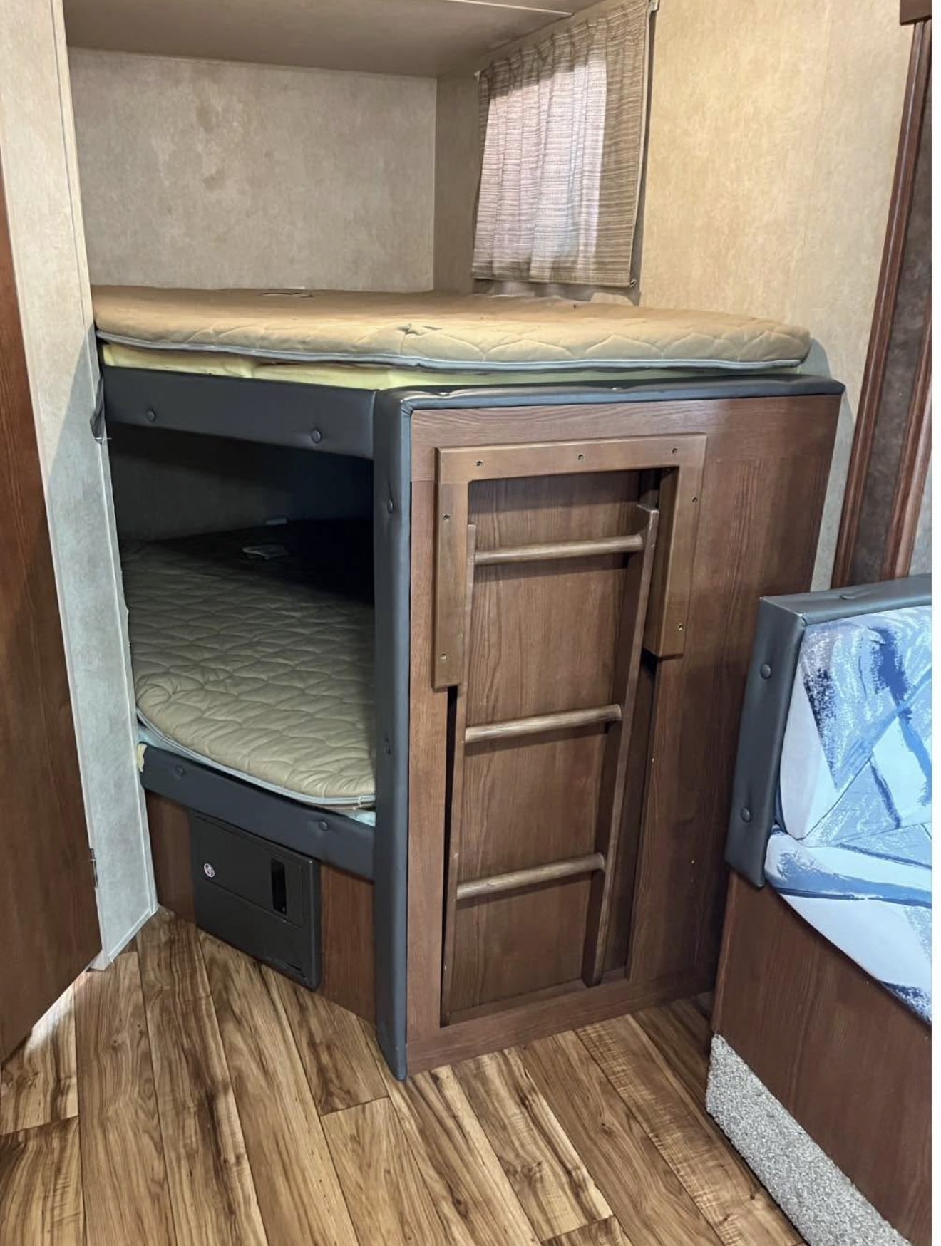 RV rental sleeping area showing two comfy bunk beds with mattresses, a stowed ladder, and wood-look flooring.. Forest River Wildwood X-Lite 2015