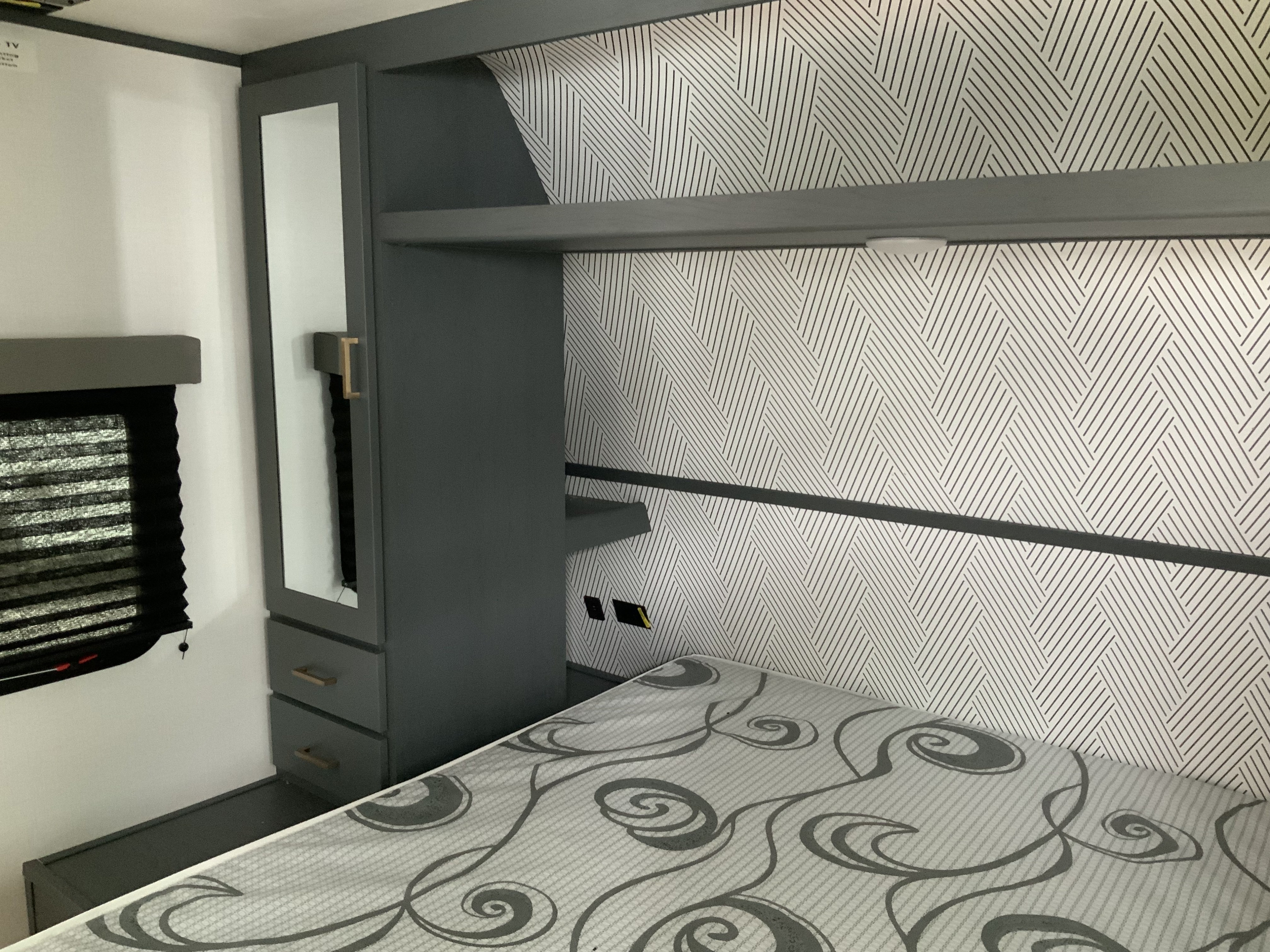 RV rental bedroom with patterned bed, modern geometric wallpaper, and a dark grey mirrored cabinet. Compact and stylish.. Keystone RV Bullet Crossfire 2022