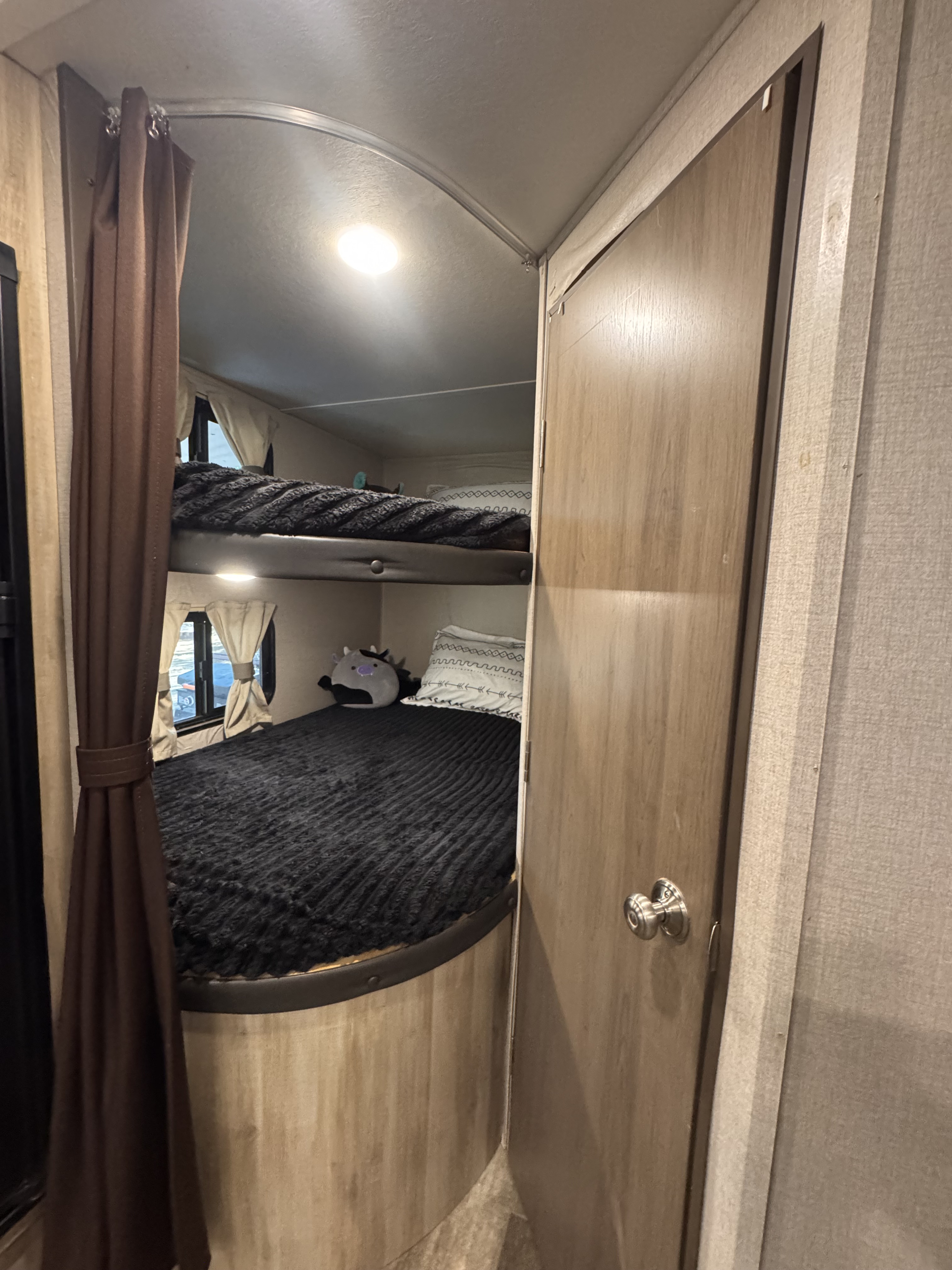 Cozy bunk beds in an RV rental, featuring dark blankets, patterned pillows, a privacy curtain, and windows.. Coachmen 184BHS 2021