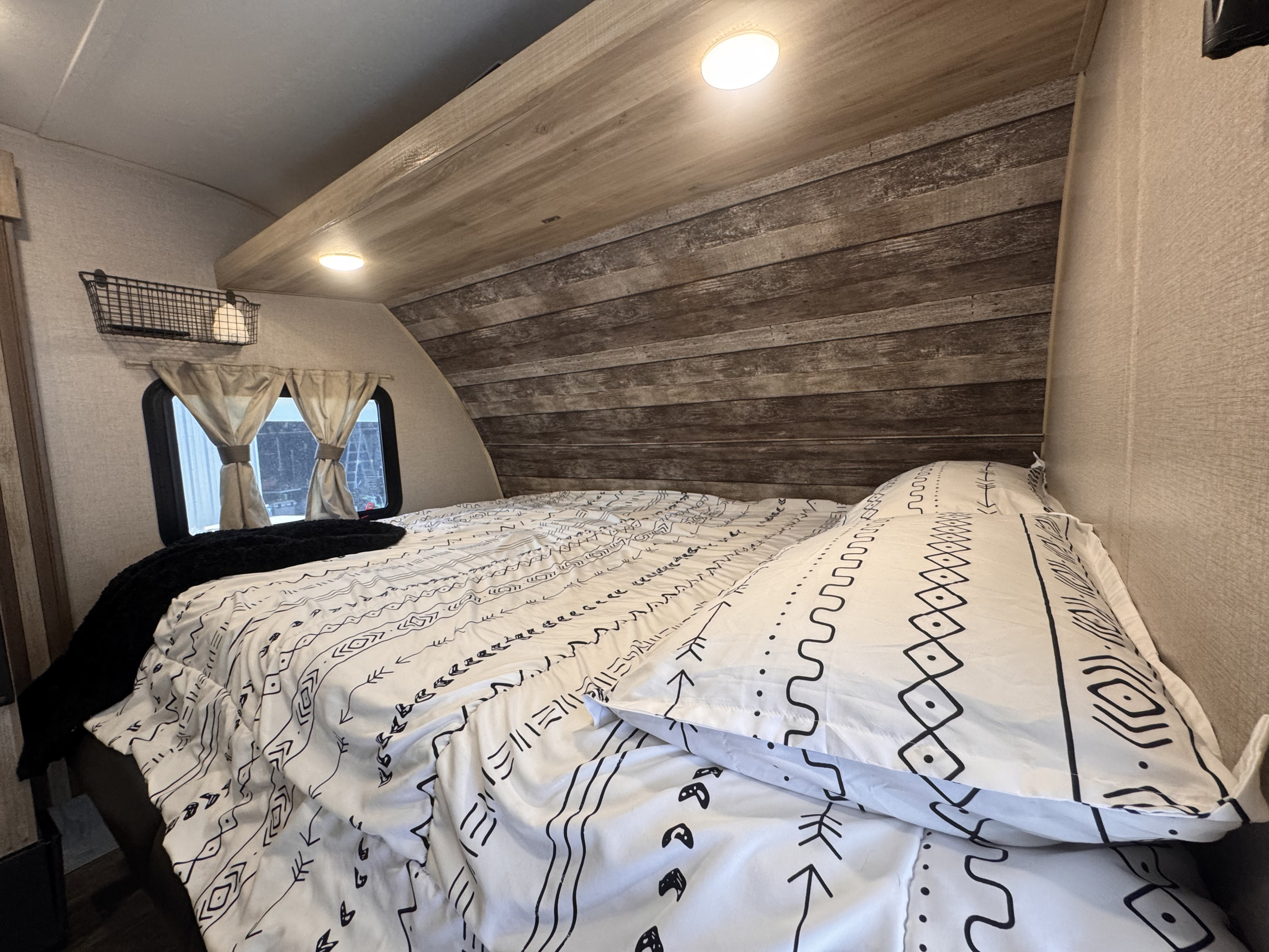 Comfortable RV rental bedroom with tribal-patterned bedding, rustic wood headboard, and convenient wall storage.. Coachmen 184BHS 2021