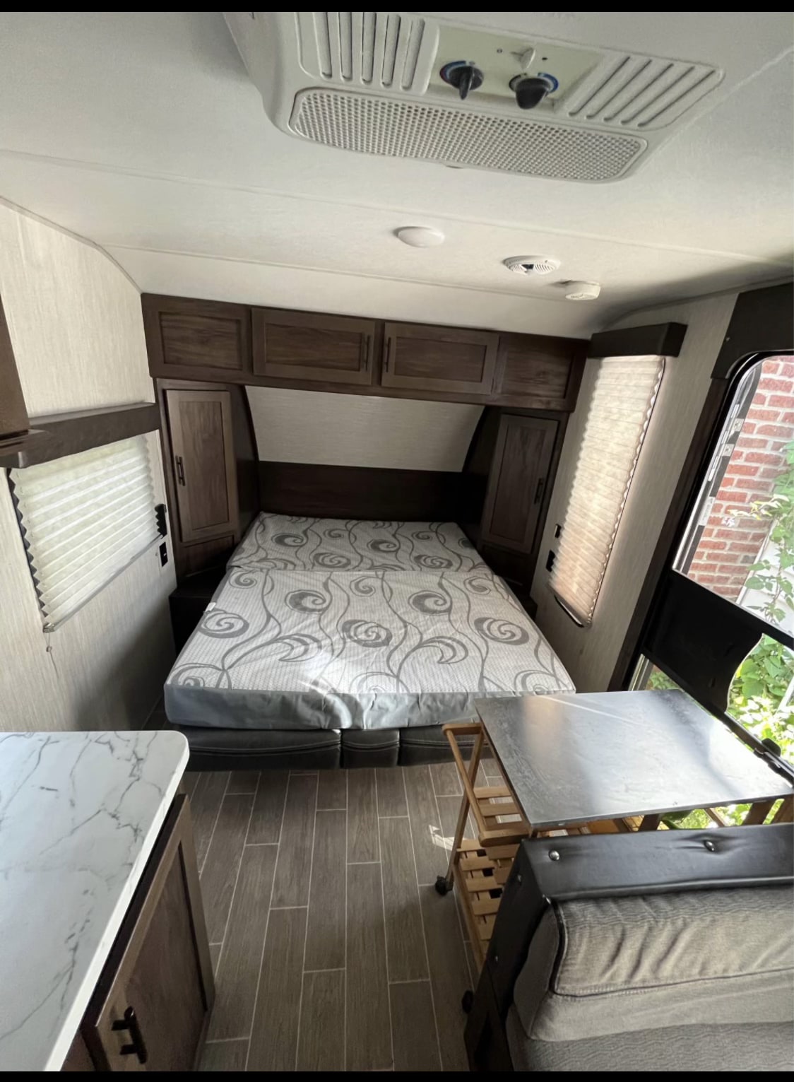 This RV rental interior features a cozy bedroom with a patterned bed, overhead cabinets, and a compact living/dining area.. Forest River Cherokee Wolf Pup 2020