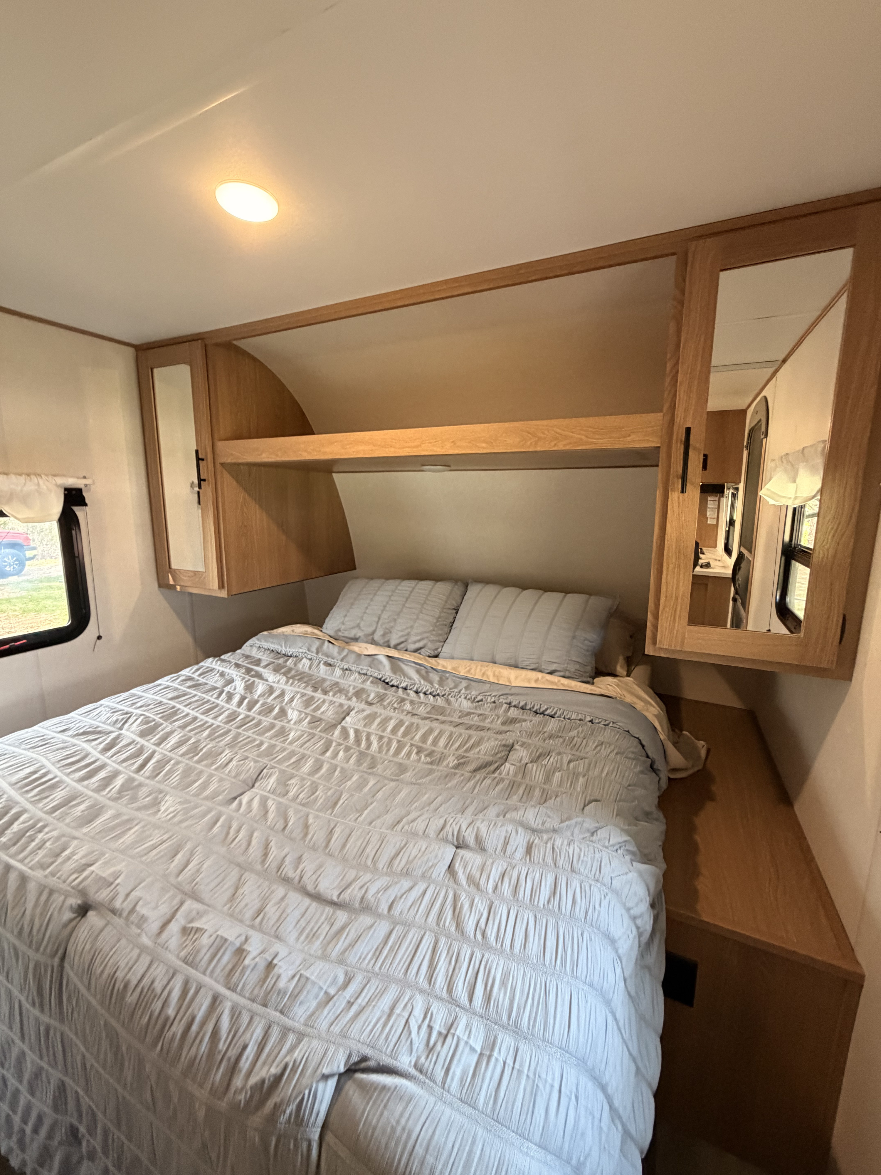 RV rental bedroom: A cozy bed with light blue bedding, overhead wood cabinets, and a window for natural light.. Avenger LE 2022