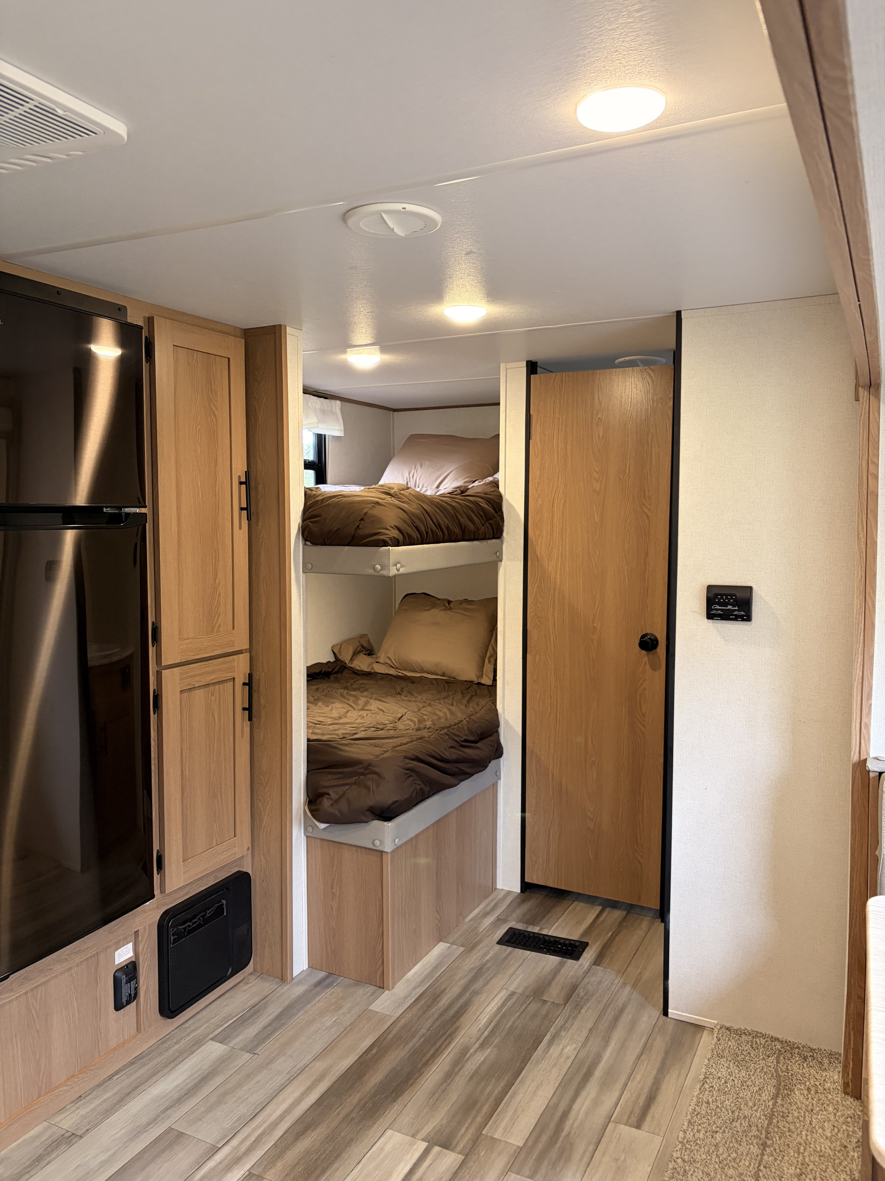 Cozy RV rental interior featuring bunk beds, refrigerator, and wood-look cabinets for family travel adventures.. Avenger LE 2022