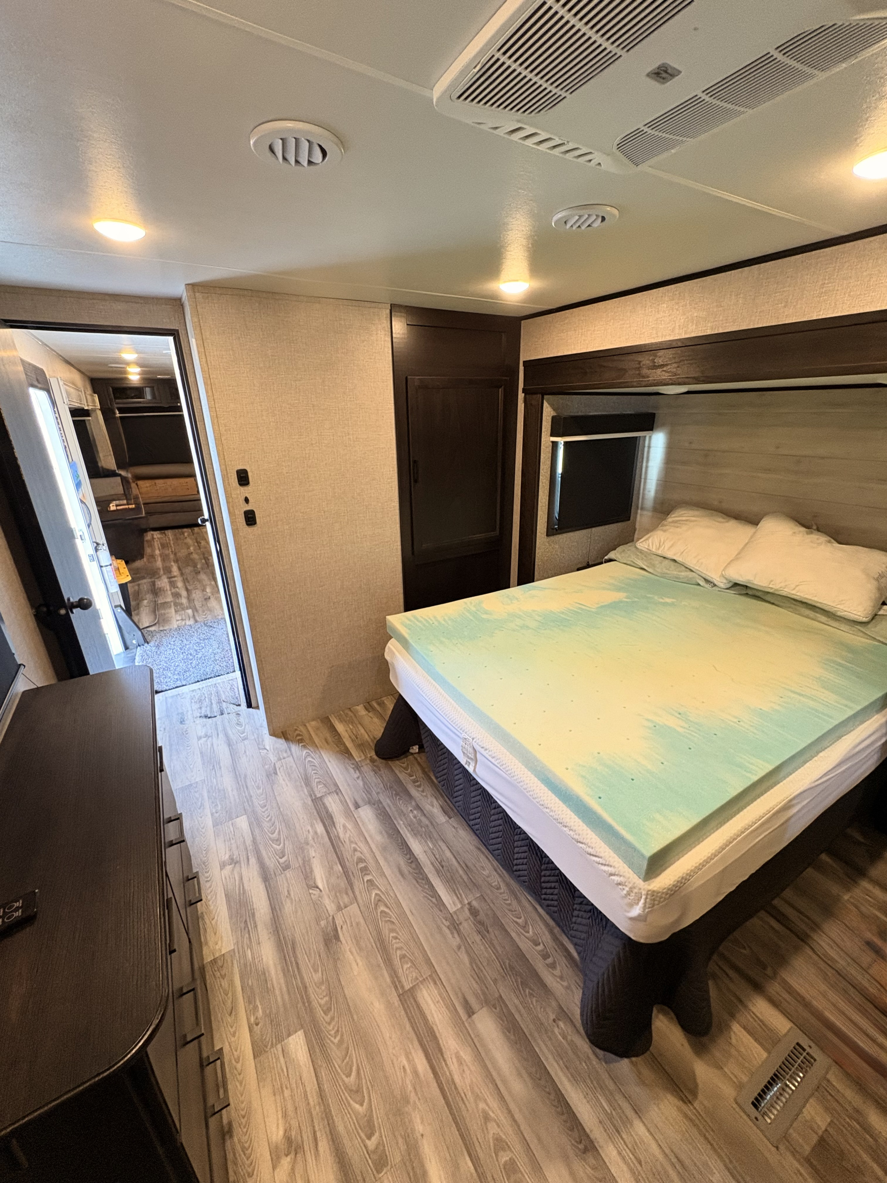 Cozy RV rental bedroom with a comfy bed, blue foam topper, wood floors, and warm lighting, perfect for your next adventure.. Jayco Eagle HT 2023