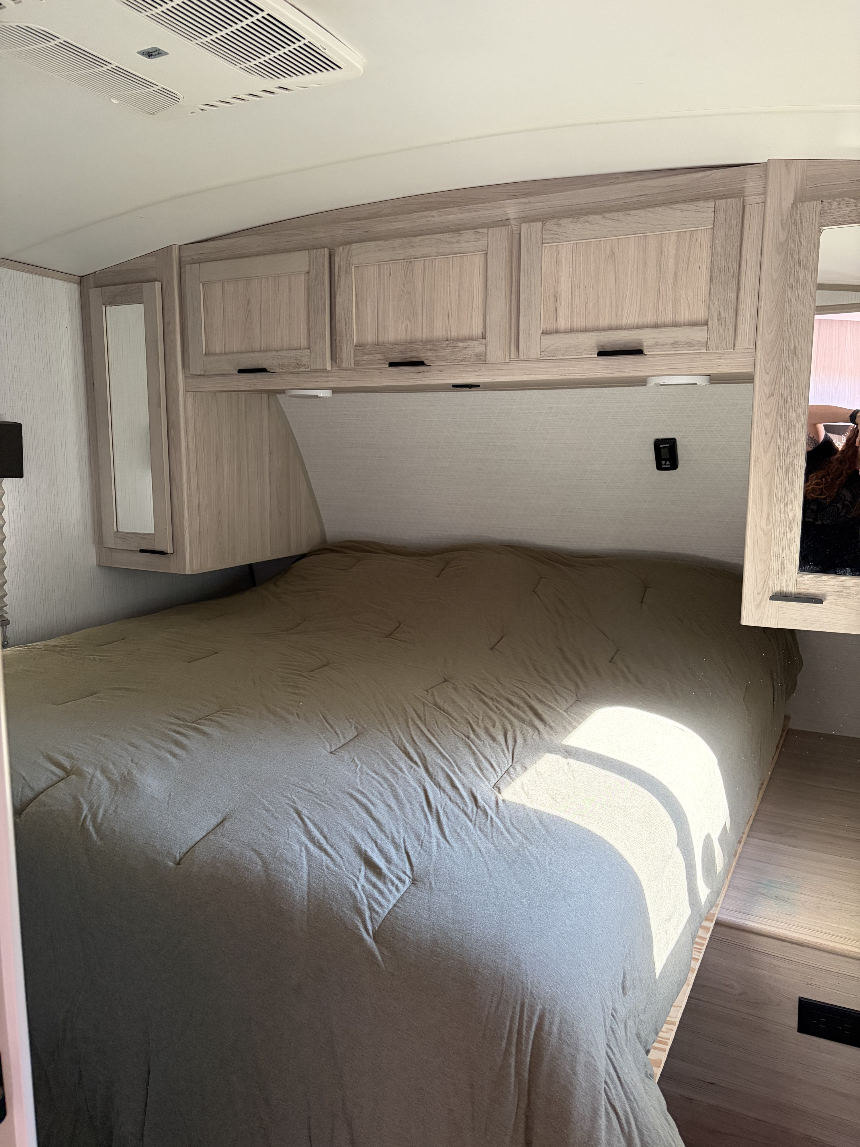 Interior of an RV rental bedroom featuring a made bed, light wood overhead cabinets, ceiling AC unit, and a mirrored side cabinet.. Cruiser RV Shadow Cruiser 2022