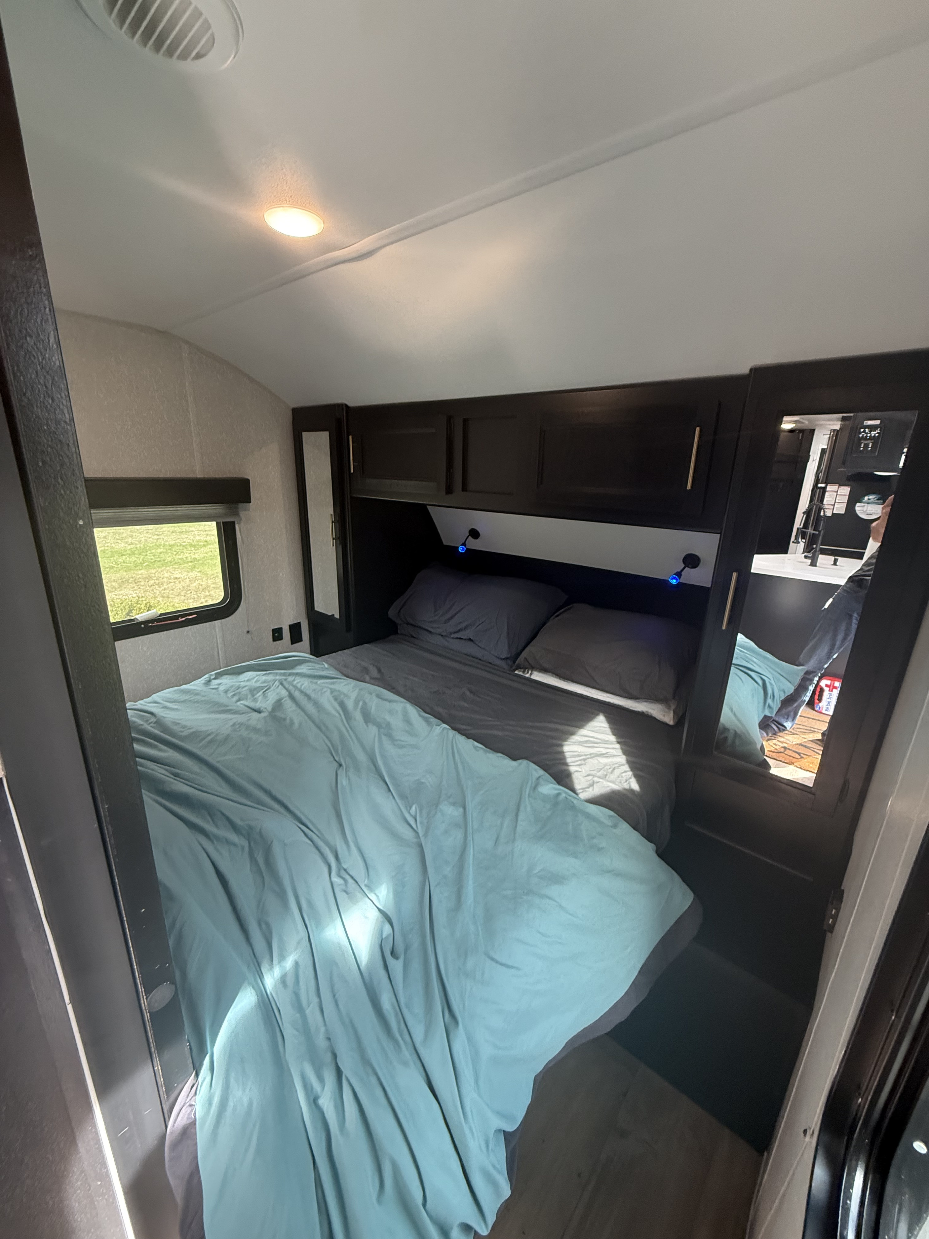 Inside an RV rental, a comfy bedroom features a bed with blue comforter, dark cabinets, a window, and mirrored closets.. Forest River Cherokee Grey Wolf 2022