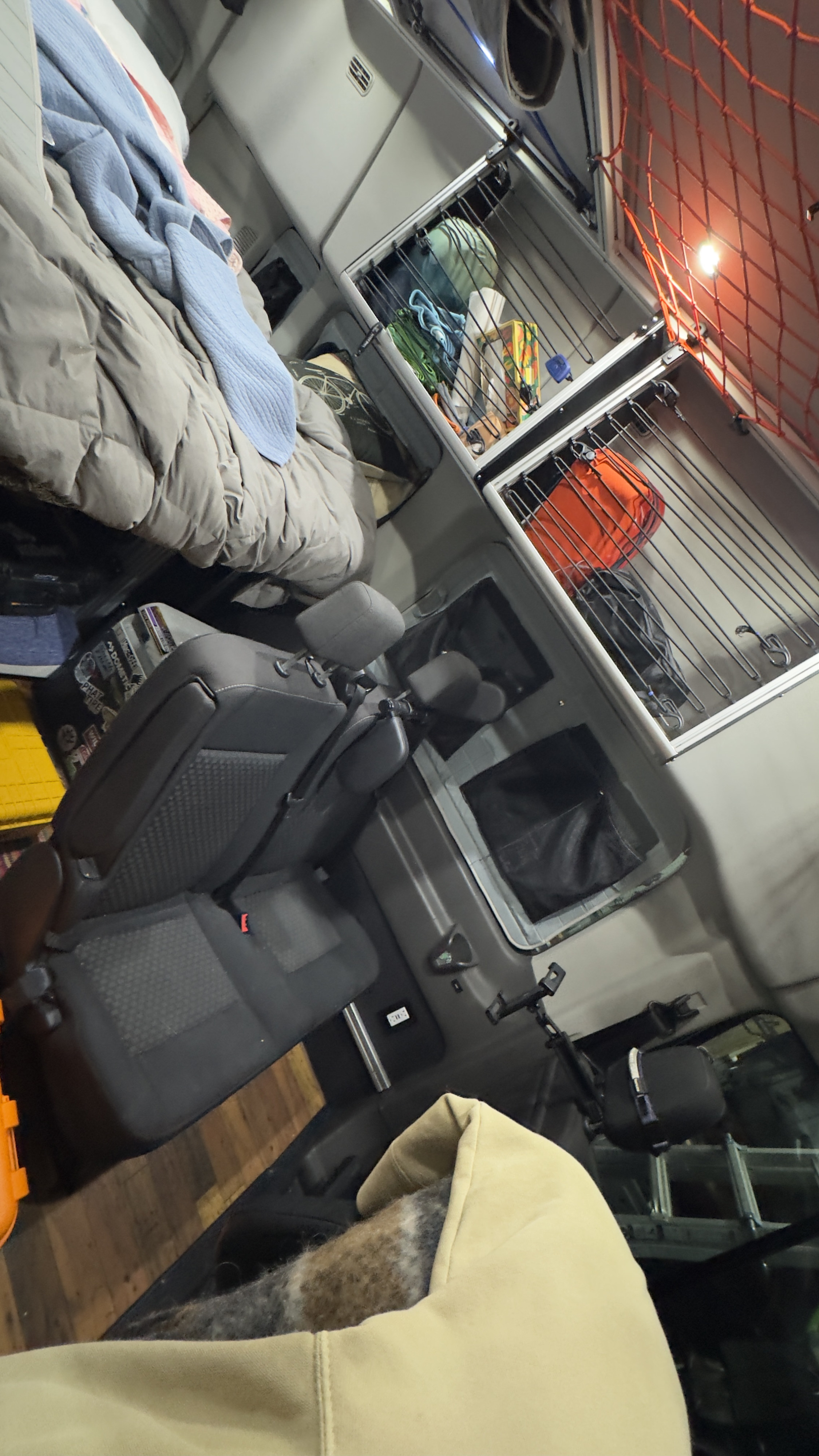 RV rental interior: cozy bed, overhead storage with gear, and vehicle seats, showcasing a compact and organized mobile living space.. Ford Custom Transit 2020
