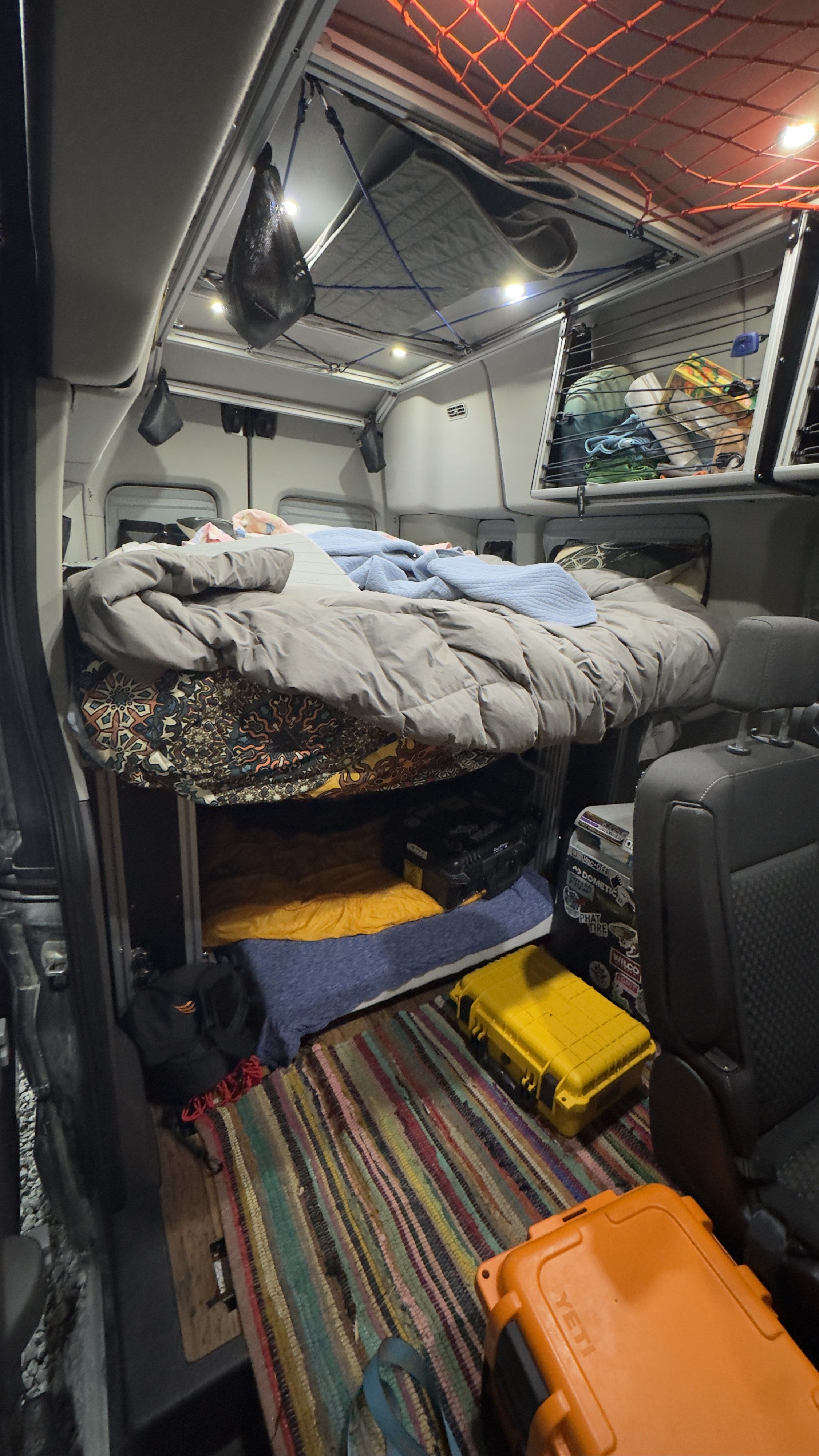Cozy RV rental interior featuring an elevated bed, ample storage, hanging nets, and floor boxes for adventure travel.. Ford Custom Transit 2020