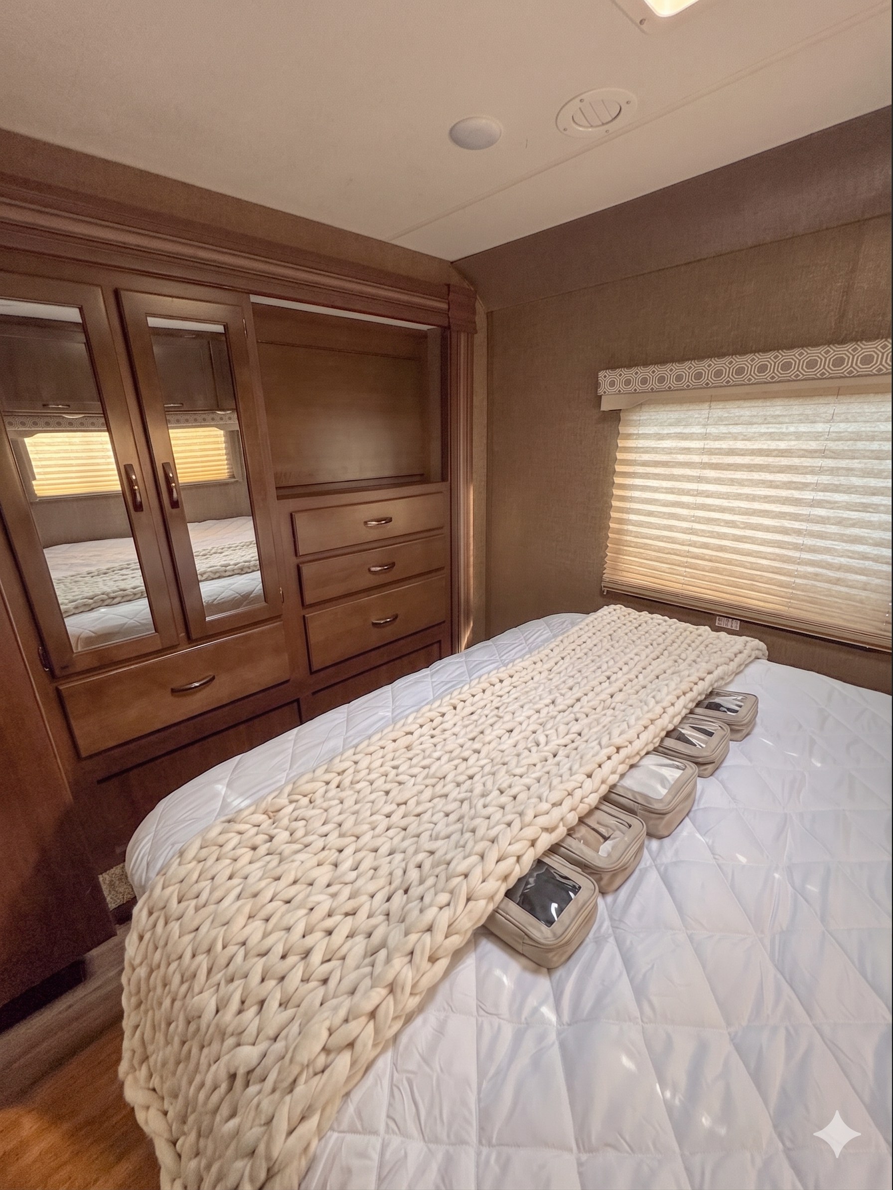 Inside an RV rental: a cozy bedroom with a bed, chunky knit cream blanket, built-in wooden wardrobe, and small travel organizers.. Thor Motor Coach 30d 2020