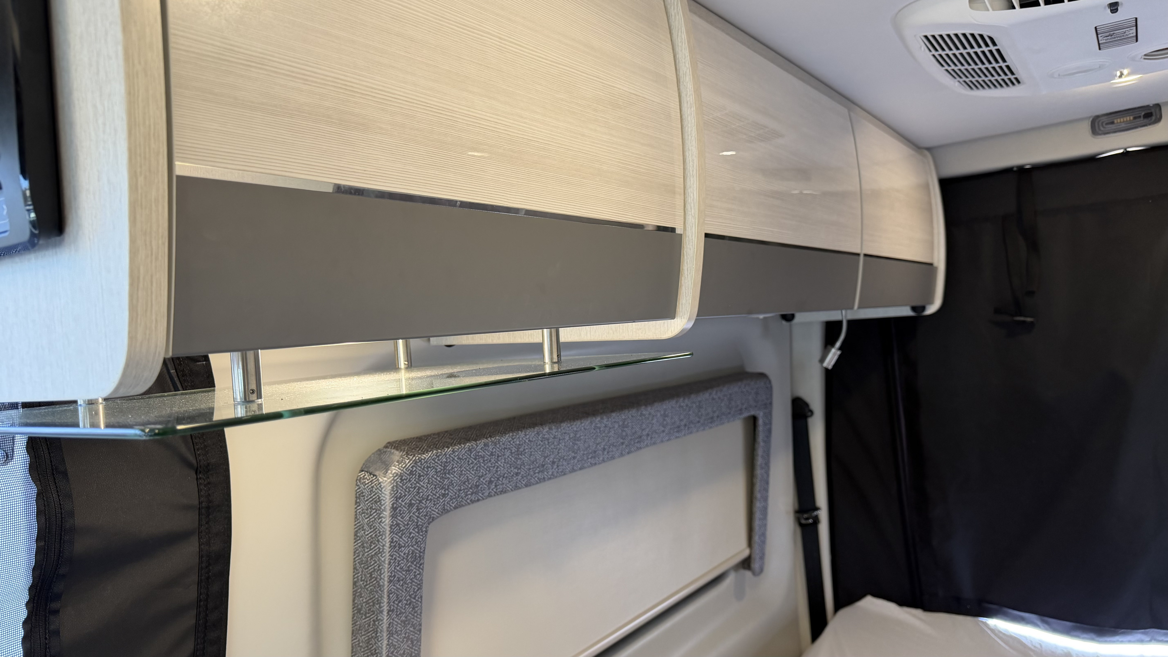 Modern rv rental interior: wood-grain overhead cabinets, glass shelf, and blackout curtains for efficient travel.. Thor Tranquility 2023