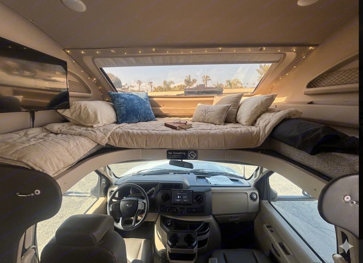 Cozy RV rental interior: cabover bed with fairy lights, TV, and the driving area below. Ready for adventure.. Entegra Coach Odyssey 2023