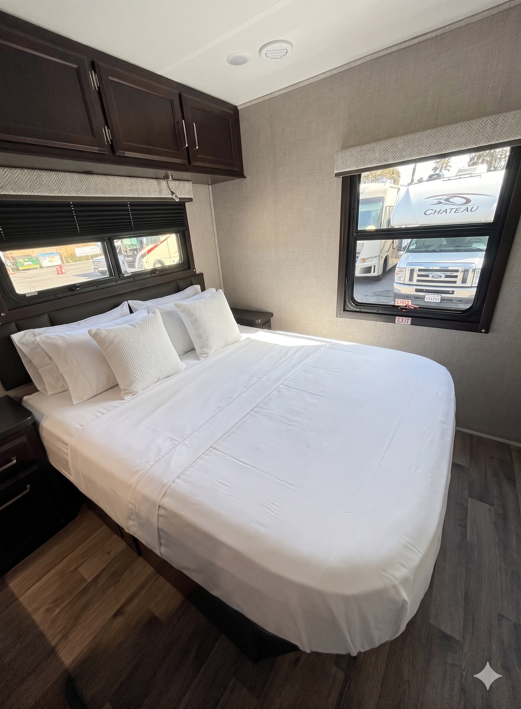 Cozy RV rental bedroom featuring a bed with crisp white linens, dark cabinets, and bright windows.. Entegra Coach Odyssey 2023