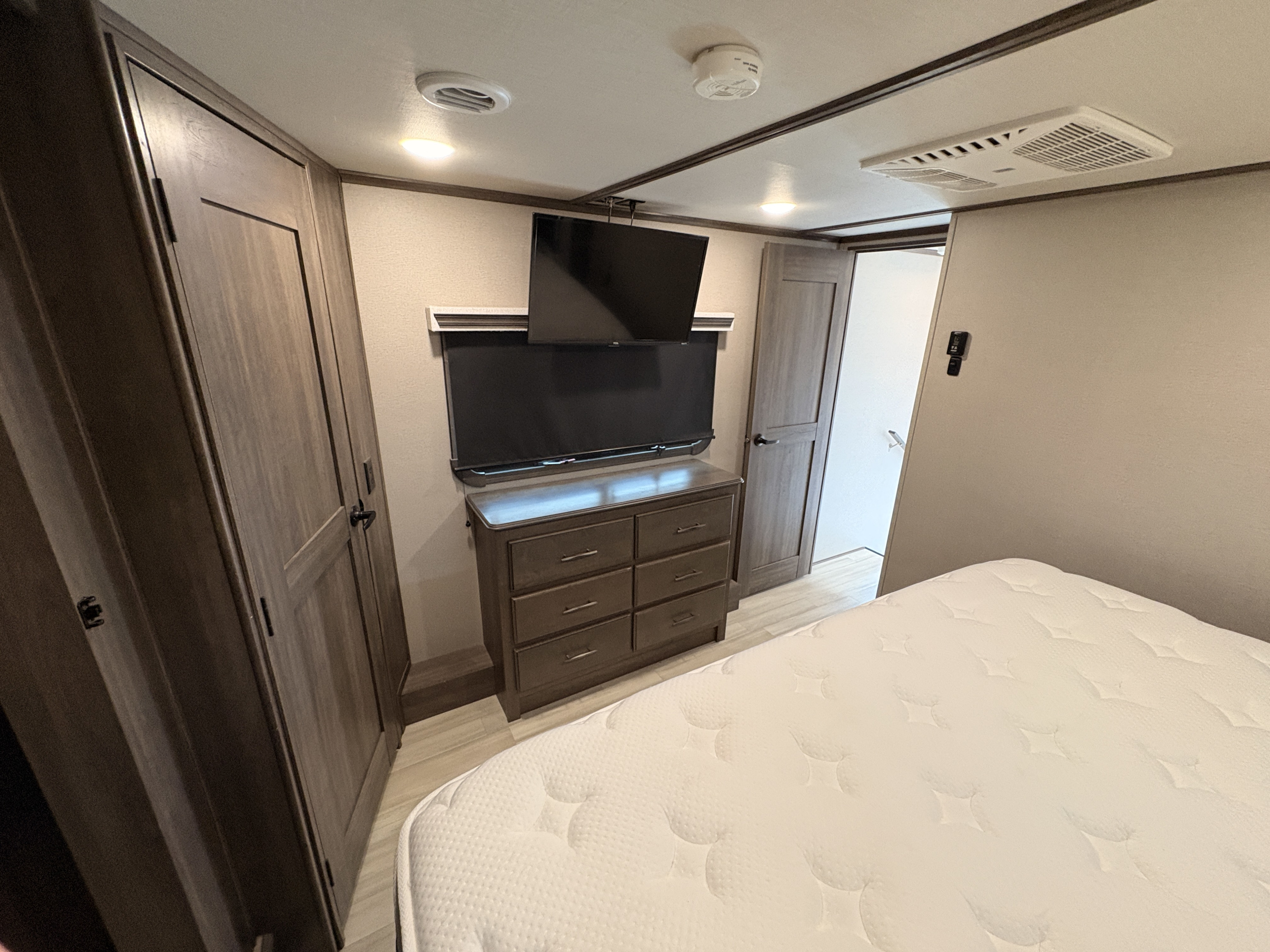 Inside an RV rental: a compact bedroom with a white bed, dresser, TV, and wardrobe, optimized for travel comfort.. Grand Design Solitude 2022