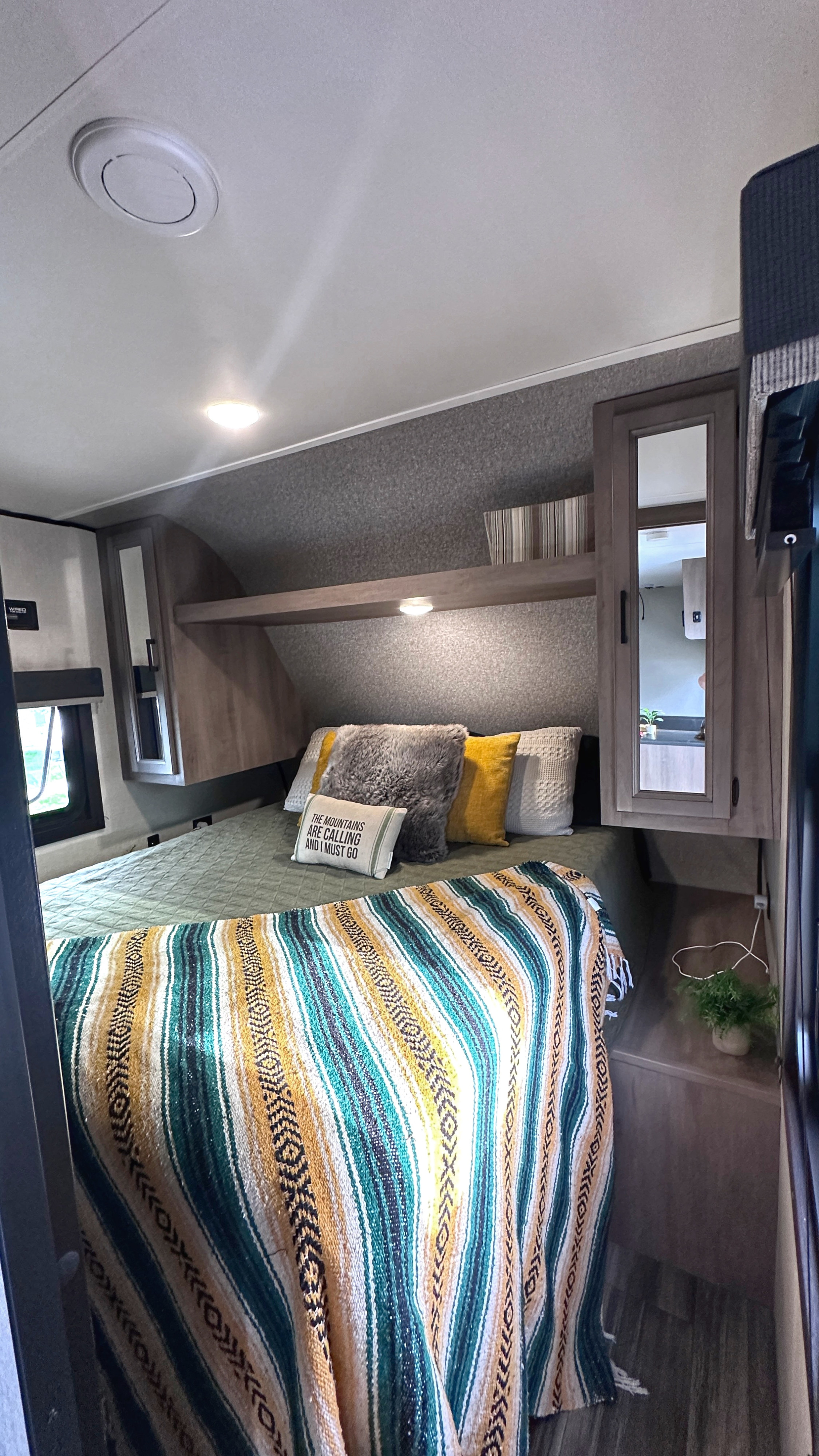 An inviting RV rental bedroom with a striped blanket, "mountains calling" pillow, and overhead cabinets for travel comfort.. Starcraft Autumn Ridge 2022