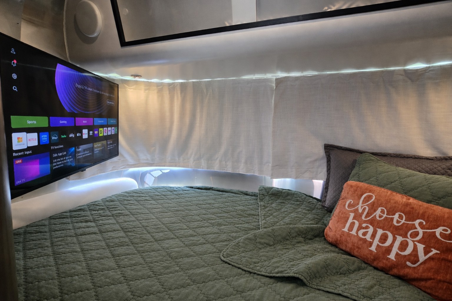 RV rental bedroom featuring a smart TV, comfy green bed with "choose happy" pillow, and warm LED lighting.. Airstream Caraval 2021