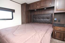 This RV rental bedroom features a comfortable bed, dark tufted headboard, and rich wood cabinetry, with a window and ample storage.. Jayco Talon Toy Hauler 2018