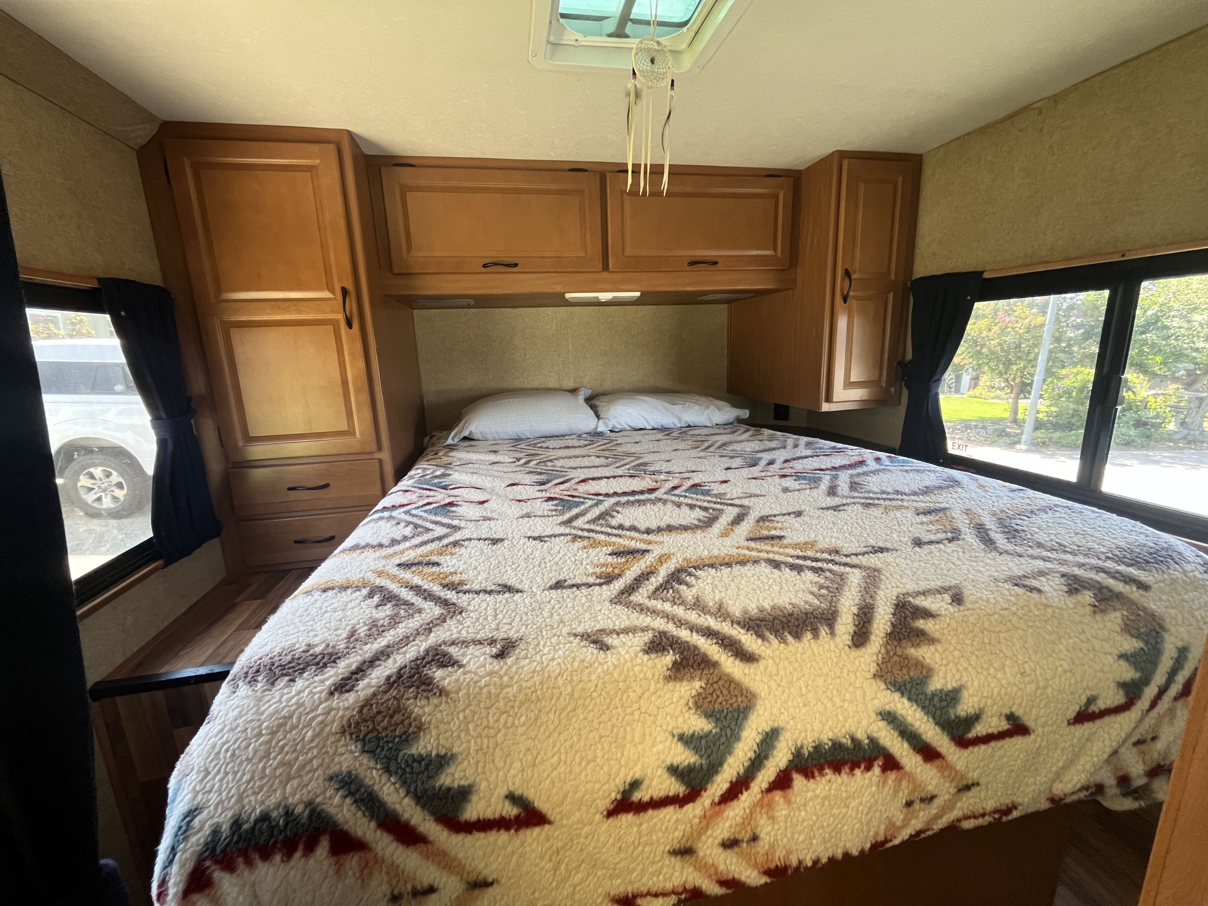 Cozy RV rental bedroom featuring a bed with a fuzzy patterned blanket, pillows, wooden cabinets, and windows.. Thor Majestic 2016