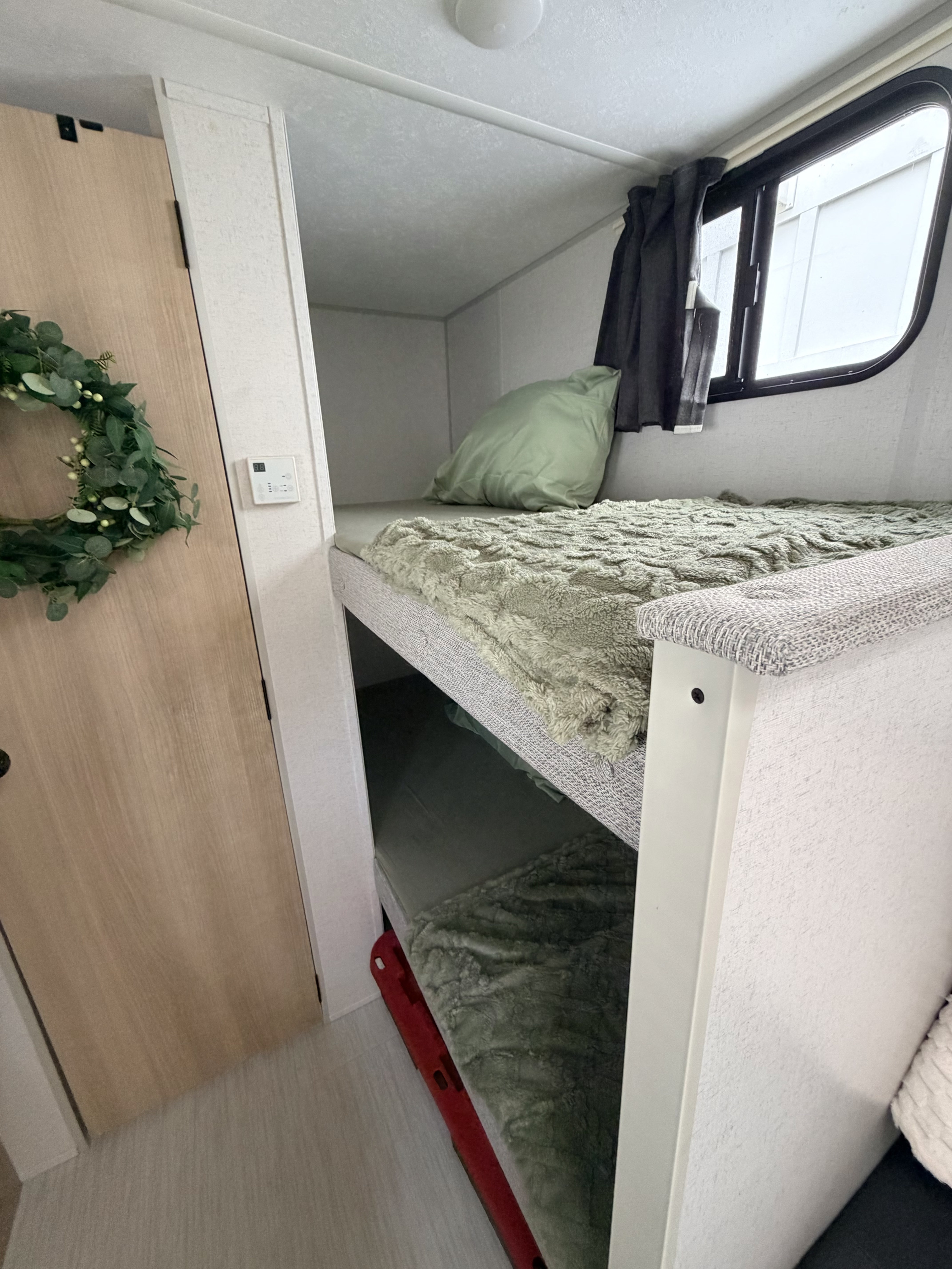 RV rental interior featuring cozy bunk beds with green blankets, a window, and a door decorated with a green wreath.. Forest River Salem FSX 2024