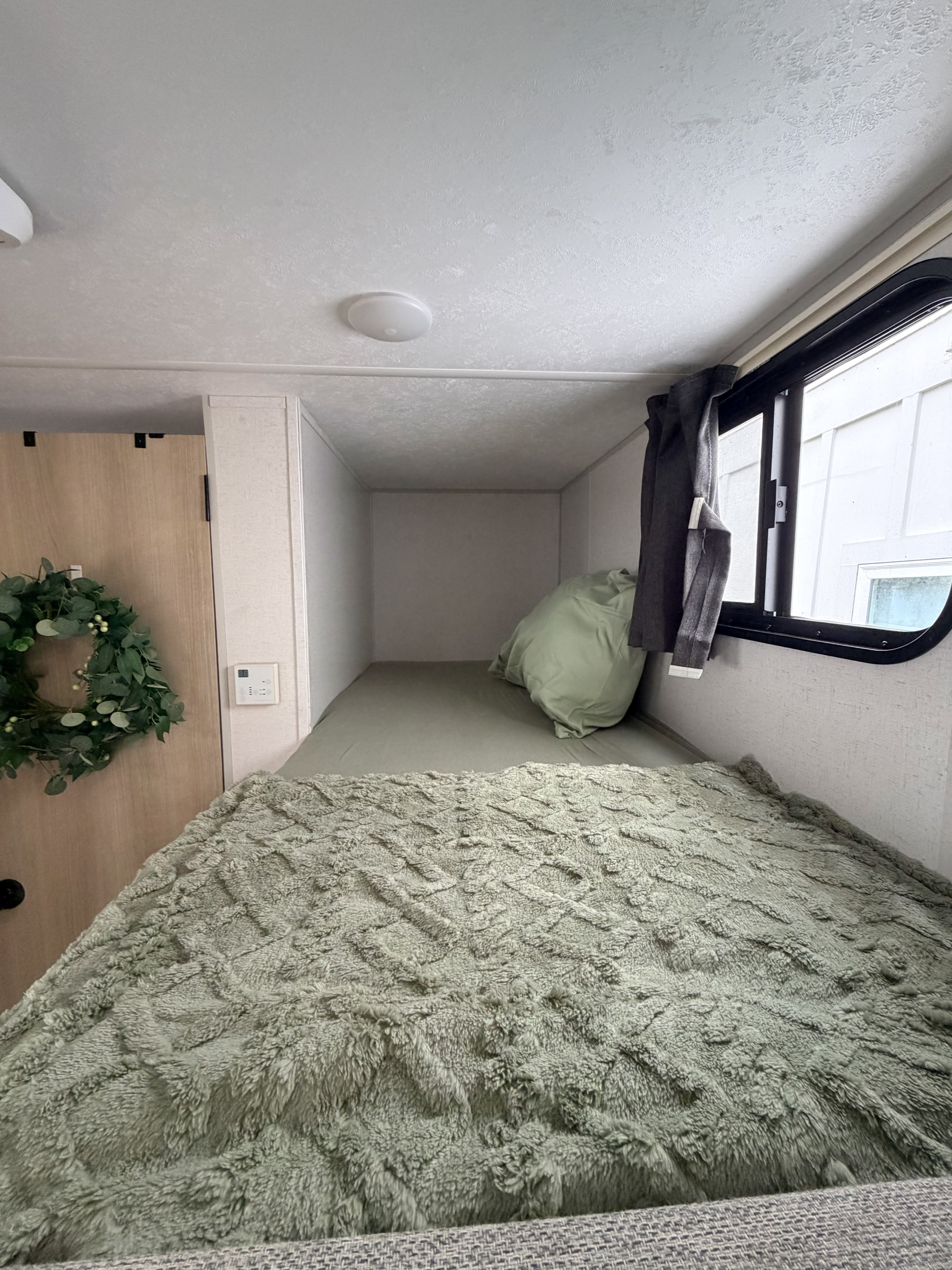 Cozy RV rental bunk bed area featuring a fluffy green blanket, an upper bunk, and a window. Ideal for compact living.. Forest River Salem FSX 2024