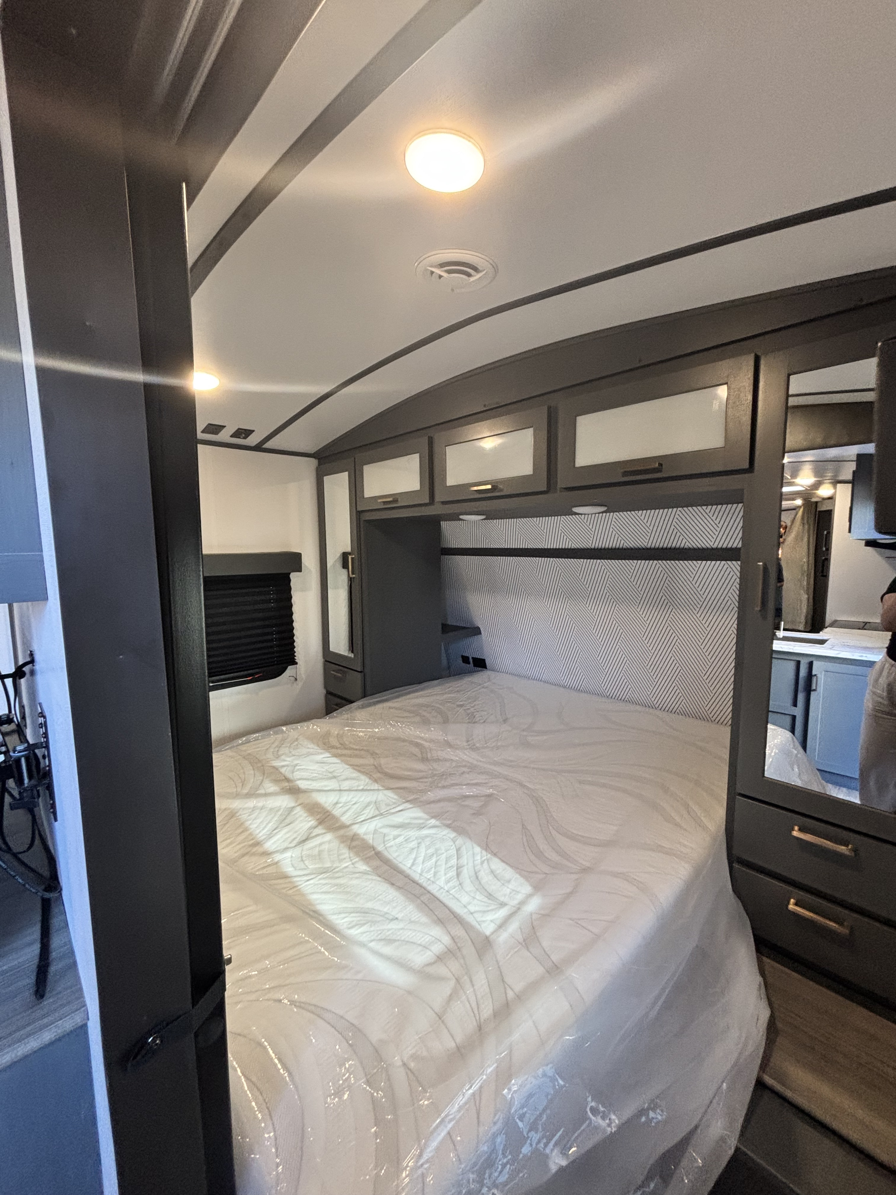 This RV rental features a modern bedroom with an unused, plastic-wrapped mattress, overhead storage, and geometric headboard.. Keystone RV Bullet Ultra Lite 2023