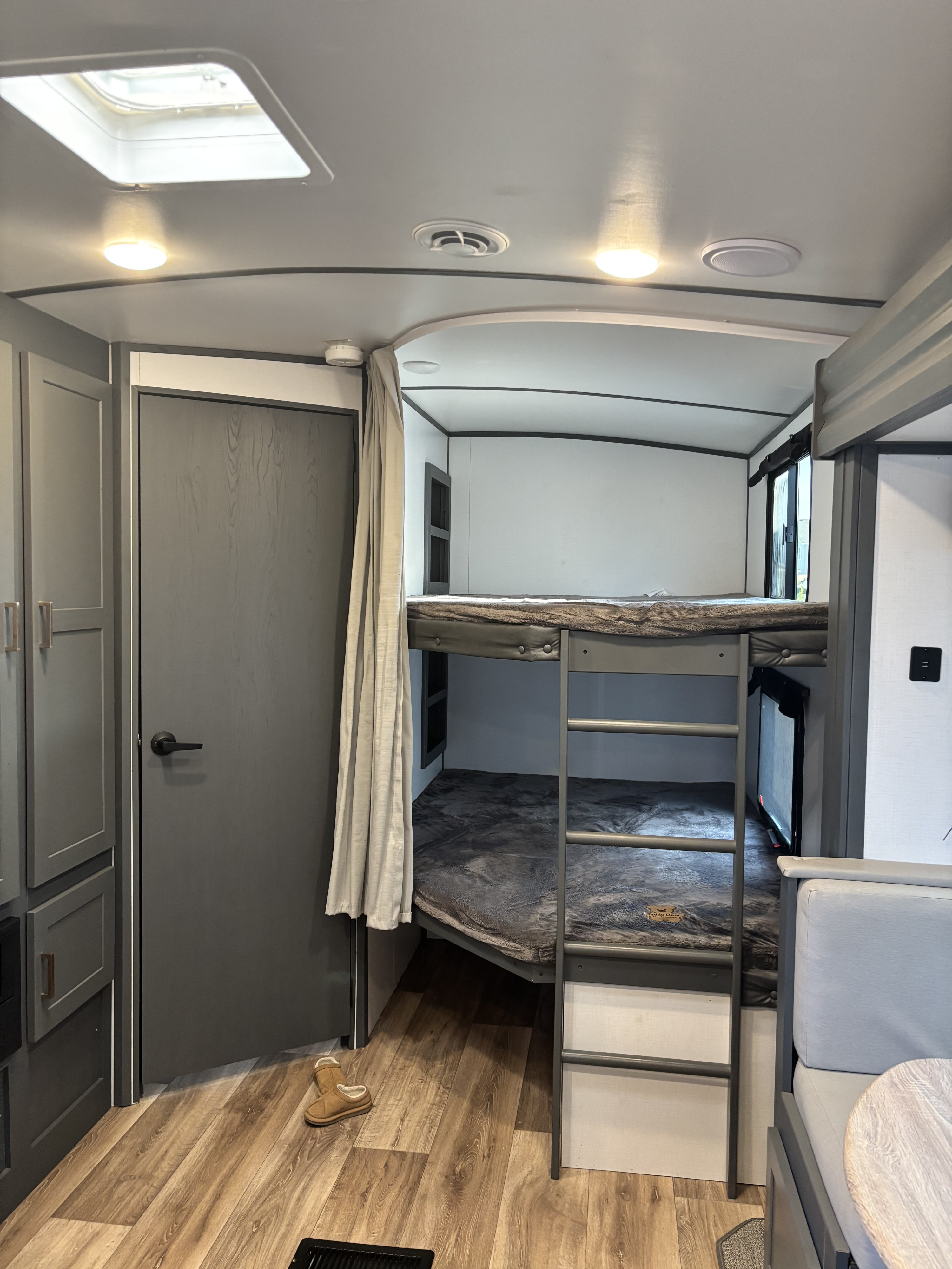 RV rental interior: Bunk beds with ladder, door, cabinets, skylight, and wood-look flooring in a camper.. Keystone RV Bullet Ultra Lite 2023