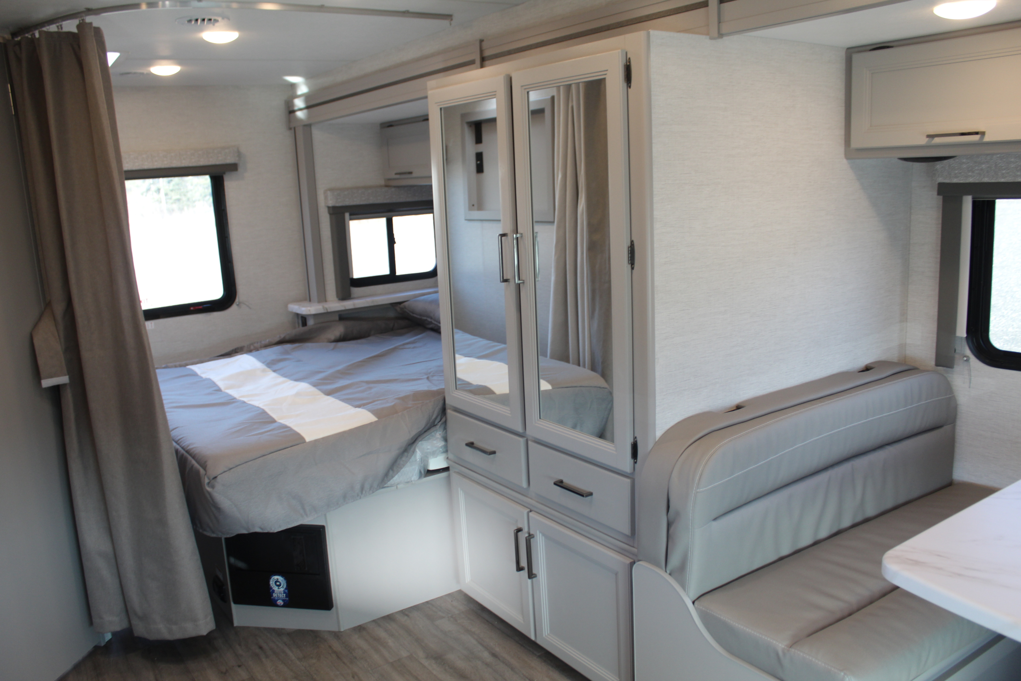 View inside an RV rental, showing a neatly made bed, mirrored cabinet, and light grey dinette bench.. Thor Motor Coach Four Winds 2025