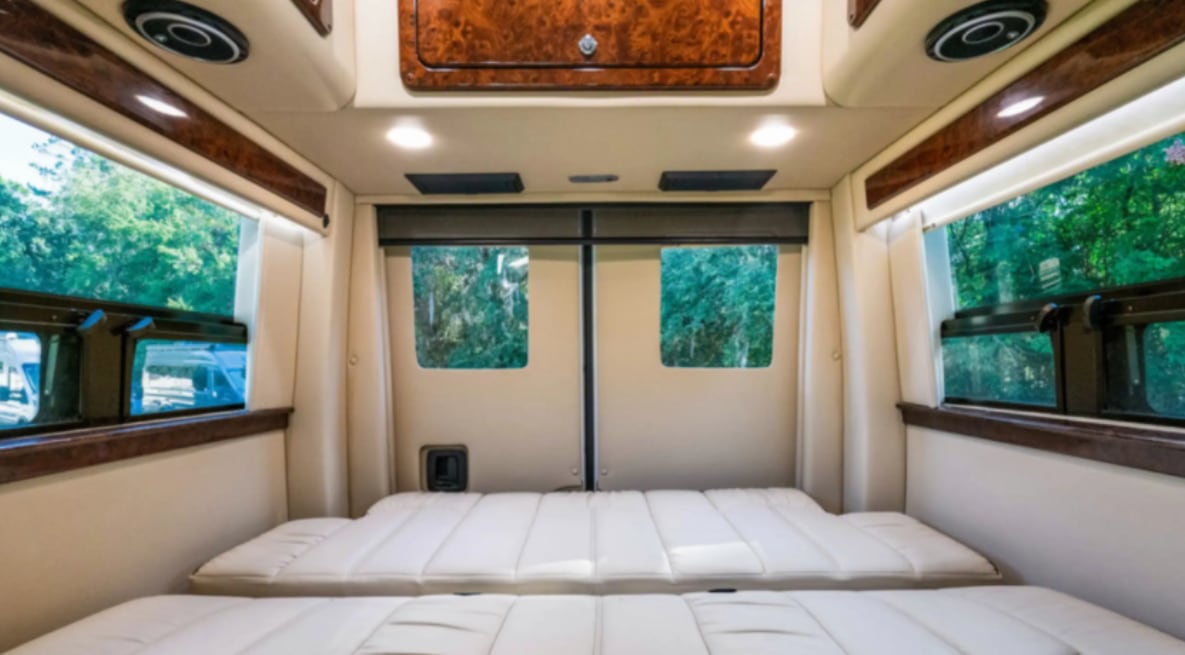 Relax in this cozy rv rental. Interior shows a comfortable cream bed/seating, with windows offering lush green views.. Midwest Automotive Designs Midwest Automotive Designs Class B 2020