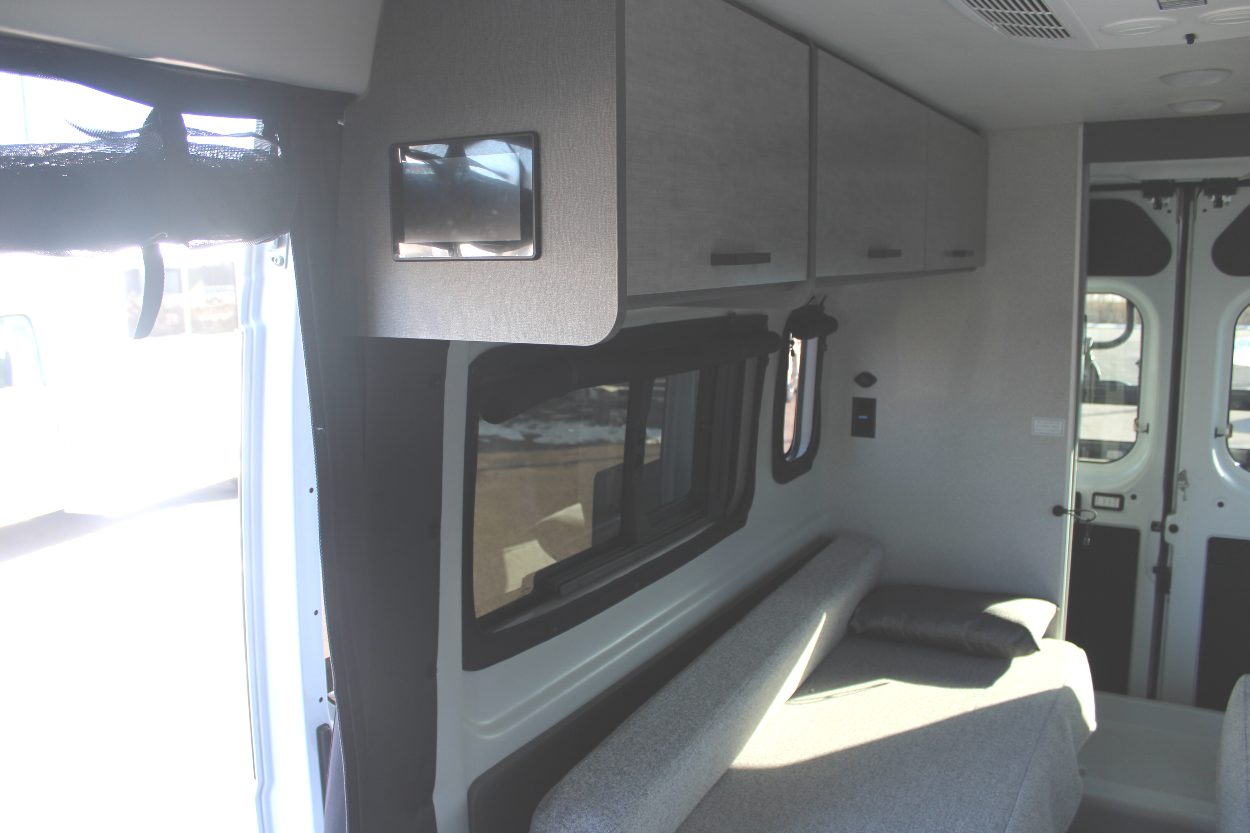 Inside an RV rental: light-filled camper van interior with grey cabinets, windows, and bench seating that converts to a bed.. Thor Motor Coach Tellaro 2026